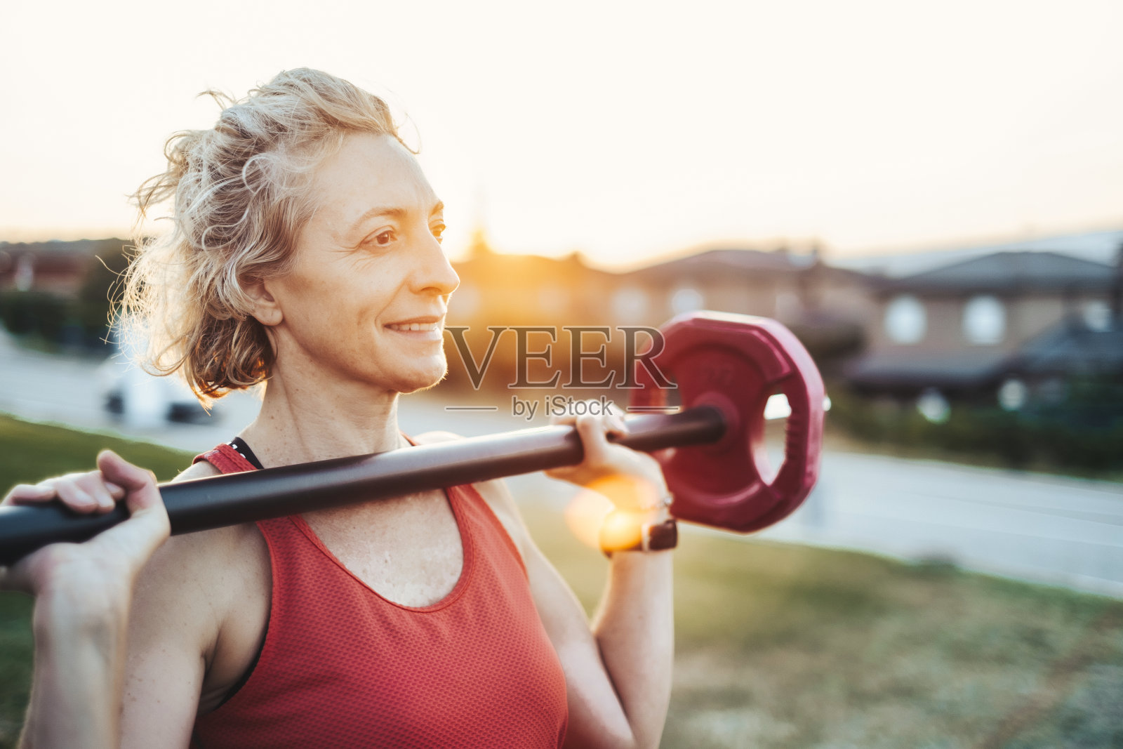 一个女人拿着一根红色的杠铃,面带微笑。照片摄影图片