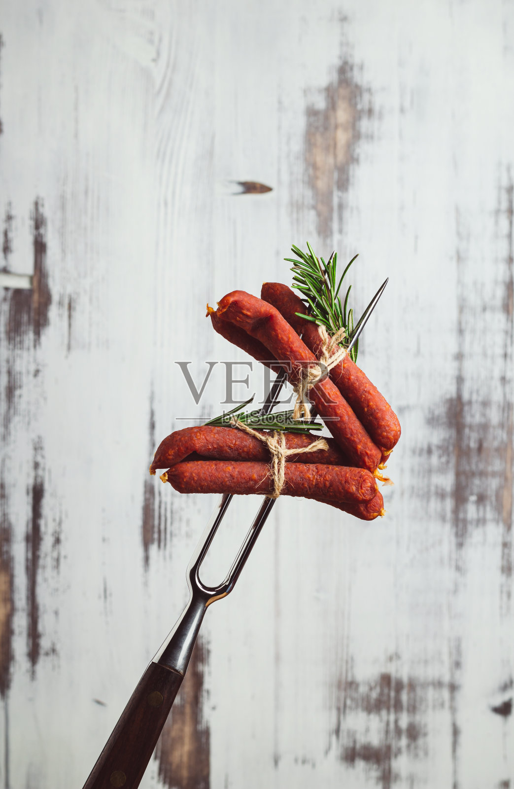 金属叉子上的干猪肉香肠。白色木制背景上的卡巴诺特写。照片摄影图片
