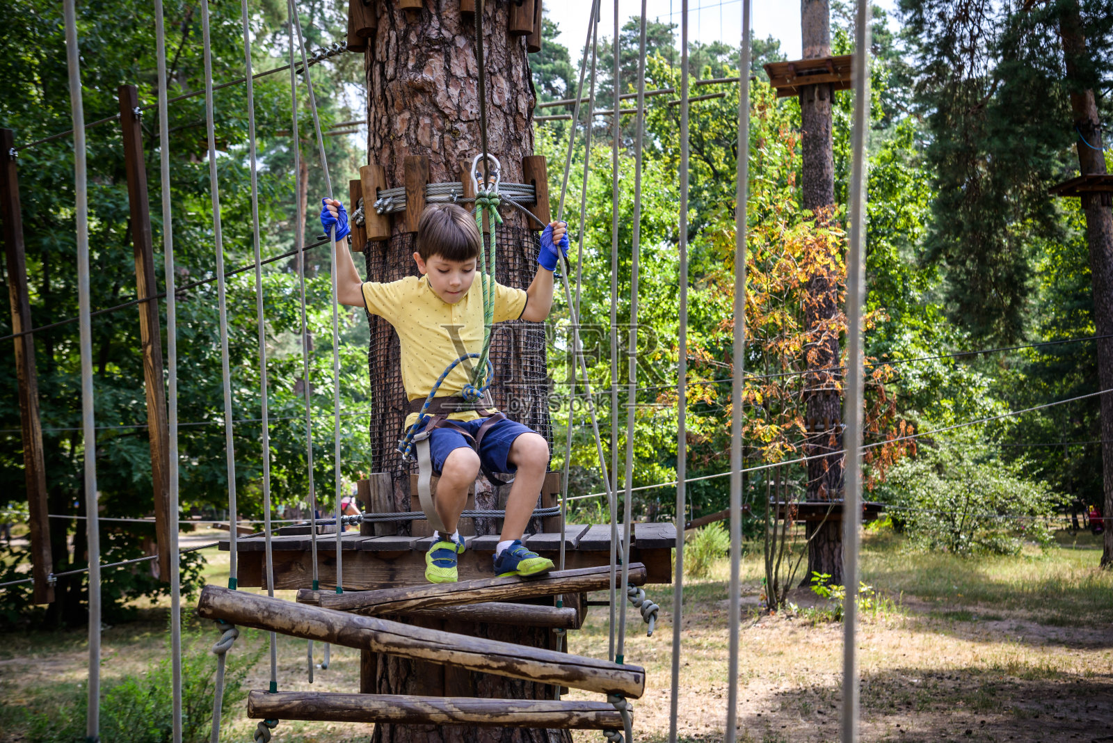 强壮兴奋的小男孩在户外绳索公园玩耍。在温暖的阳光下,穿着休闲服和运动鞋的高加索孩子。积极的休闲时间与孩子的概念照片摄影图片