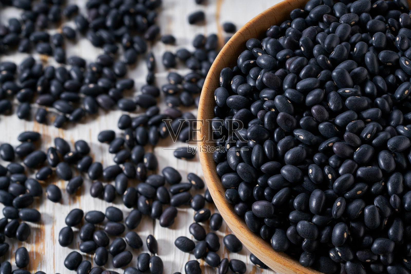 有机黑豆散落在木碗上的轻桌上,选择性聚焦。照片摄影图片