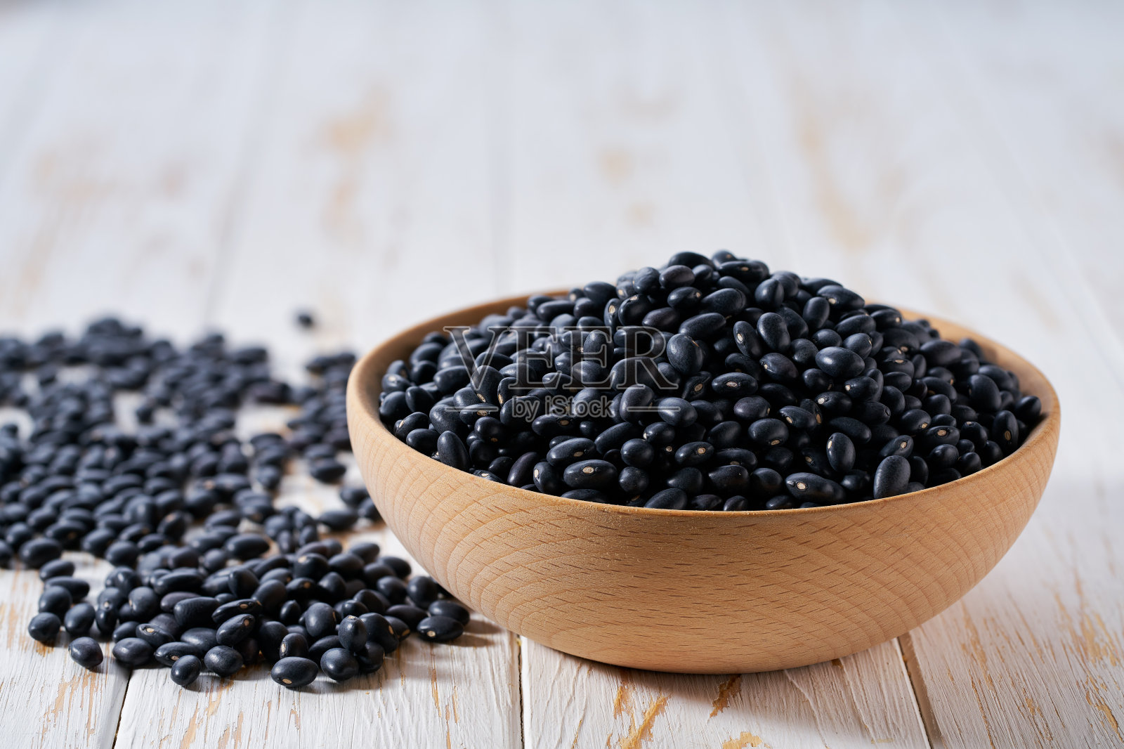 白色木桌上的木碗里装着有机黑豆。照片摄影图片