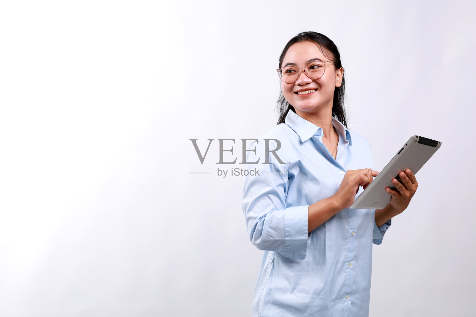 微笑忙碌的年轻亚洲商业女经理使用平板电脑,快乐的商业女执行官看着空白的空间,站在白色的背景照片摄影图片