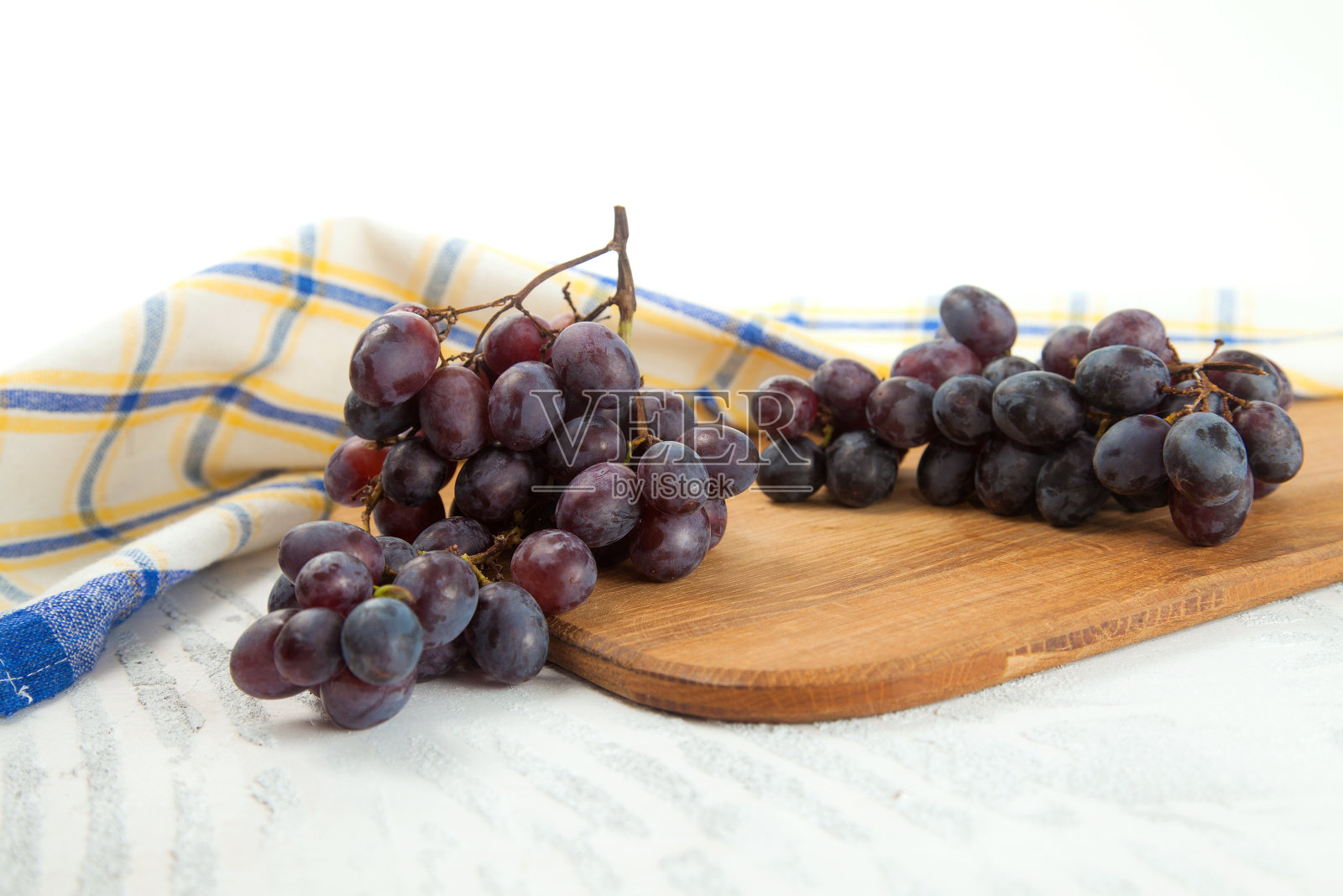 砧板与一束有机黑葡萄在白色木制背景。照片摄影图片