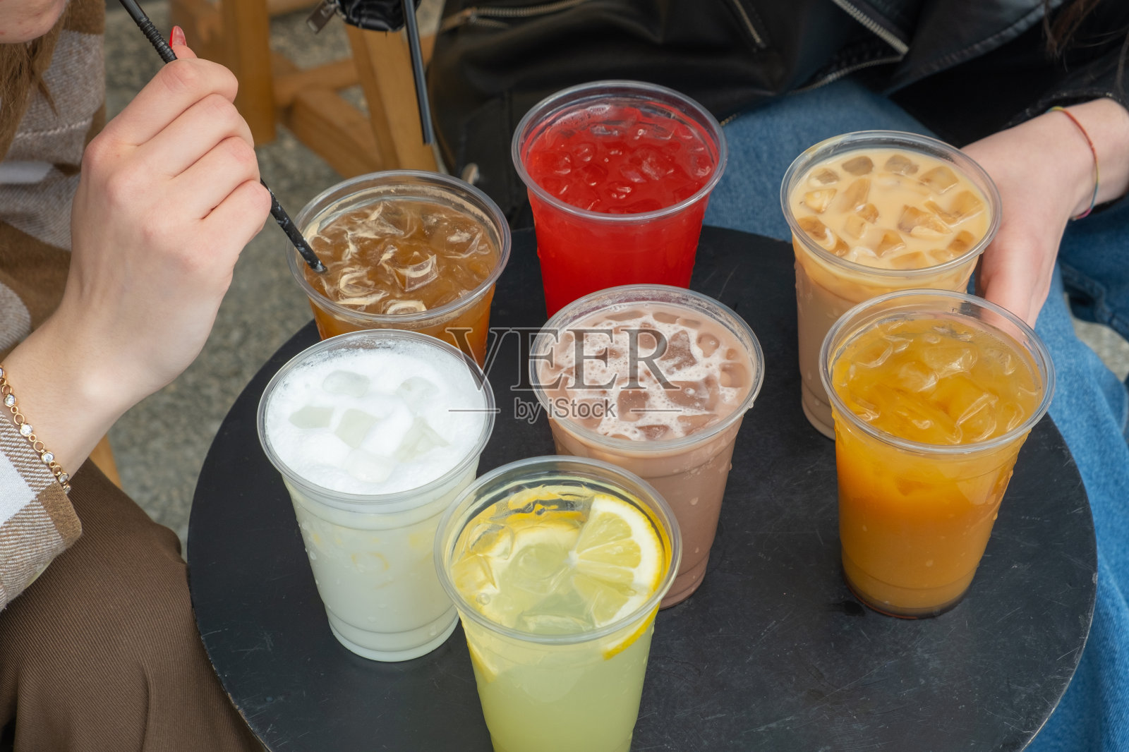 两个人和外带的夏日饮料,桌上放着冰块。柠檬水和鸡尾酒。照片摄影图片