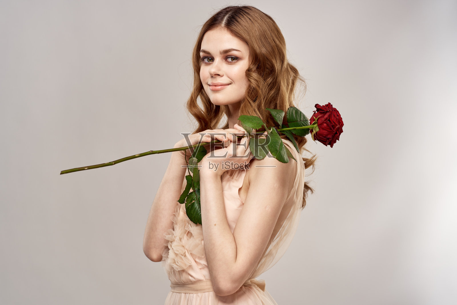 在米色的背景上,一个美丽的女人拿着一朵红玫瑰的肖像照片摄影图片