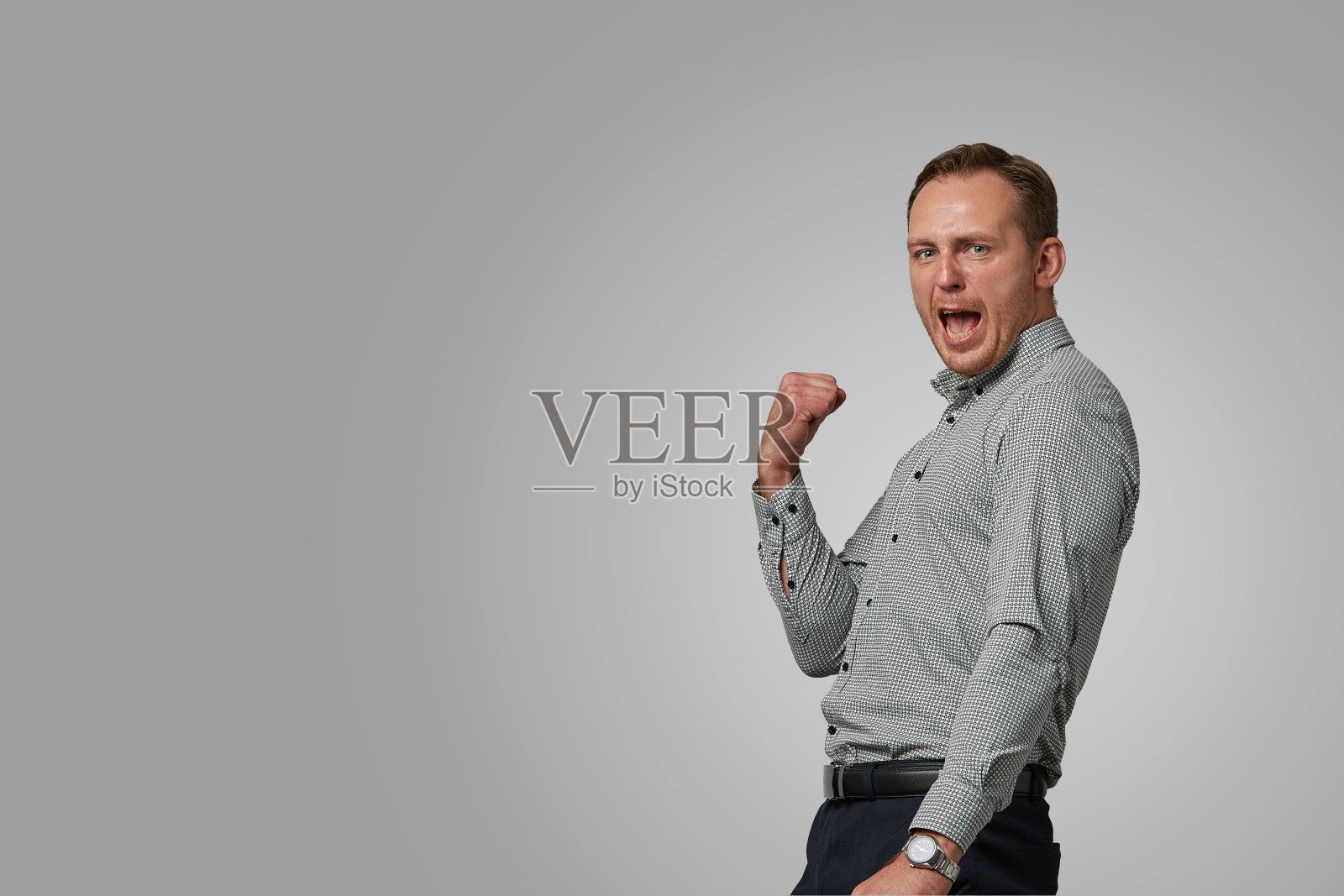 快乐兴奋的年轻人穿着灰色套头衫尖叫和庆祝他的成功在白色的背景。情绪化,勇敢面对。孤立的白色背景复制空间广告和商业设计。照片摄影图片