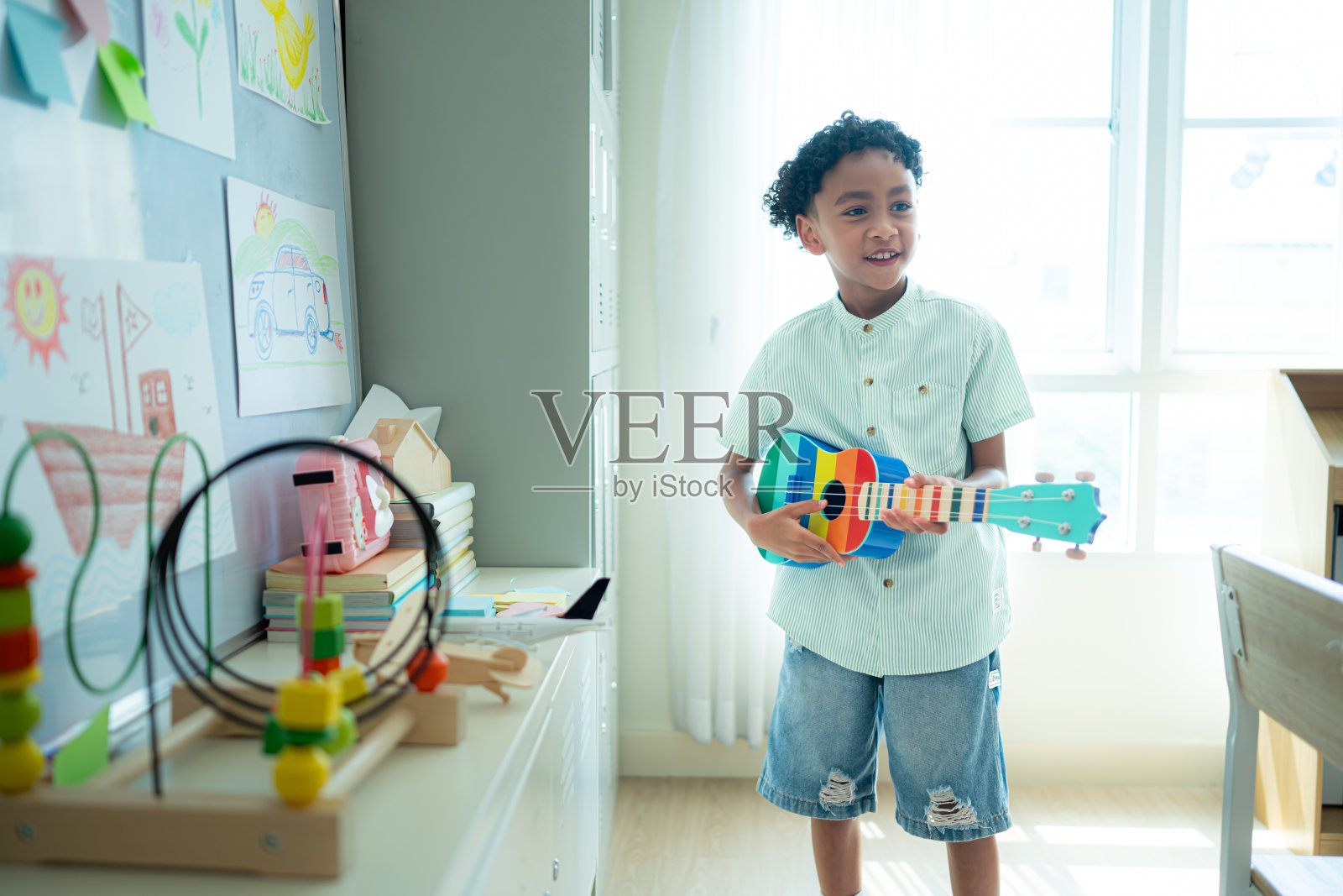 小艺术家一边在教室后面弹着尤克里里,一边等着朋友们走进教室照片摄影图片