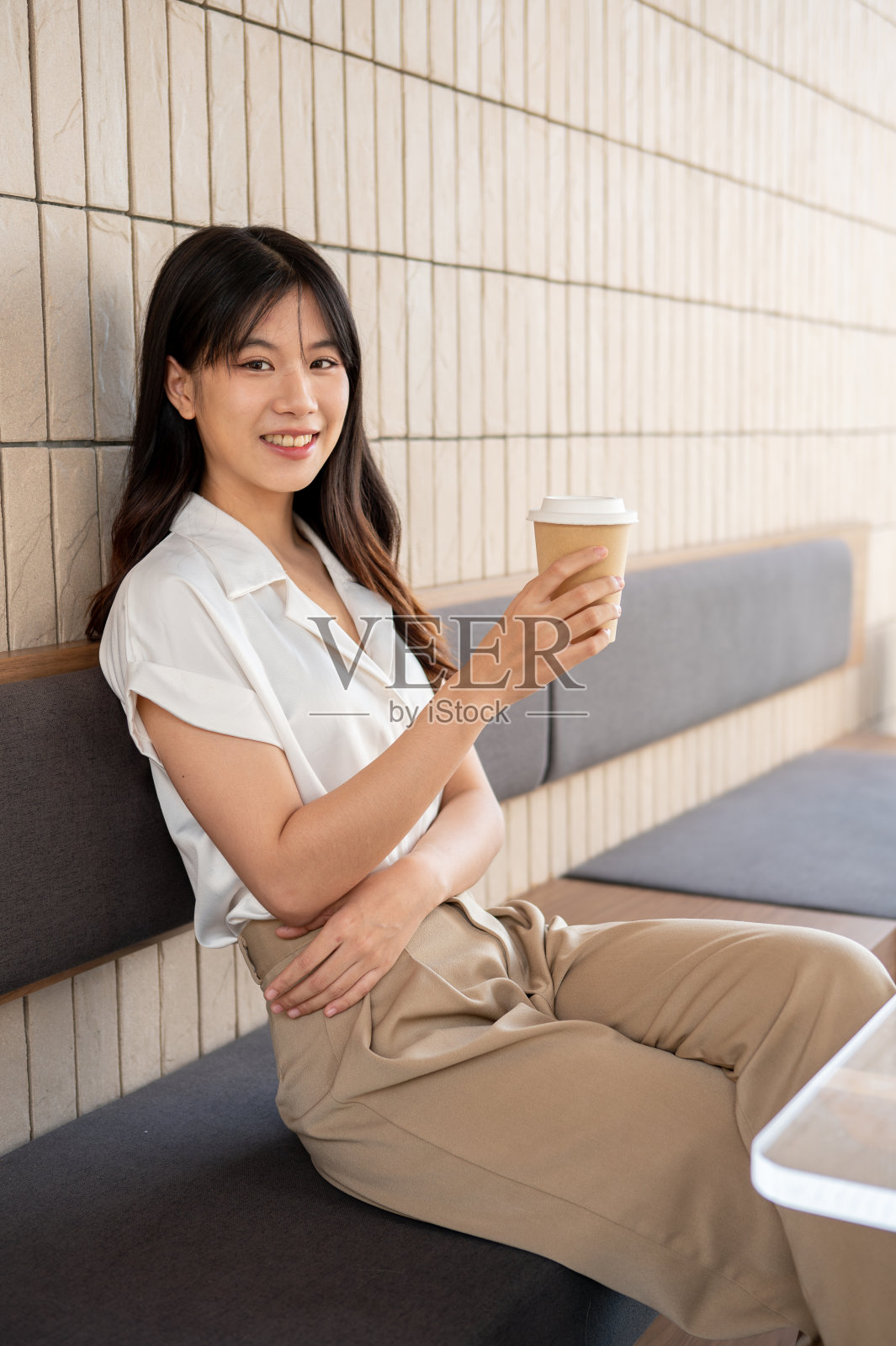 一个迷人的亚洲女人坐在咖啡店里,手里拿着咖啡杯,对着镜头微笑。照片摄影图片