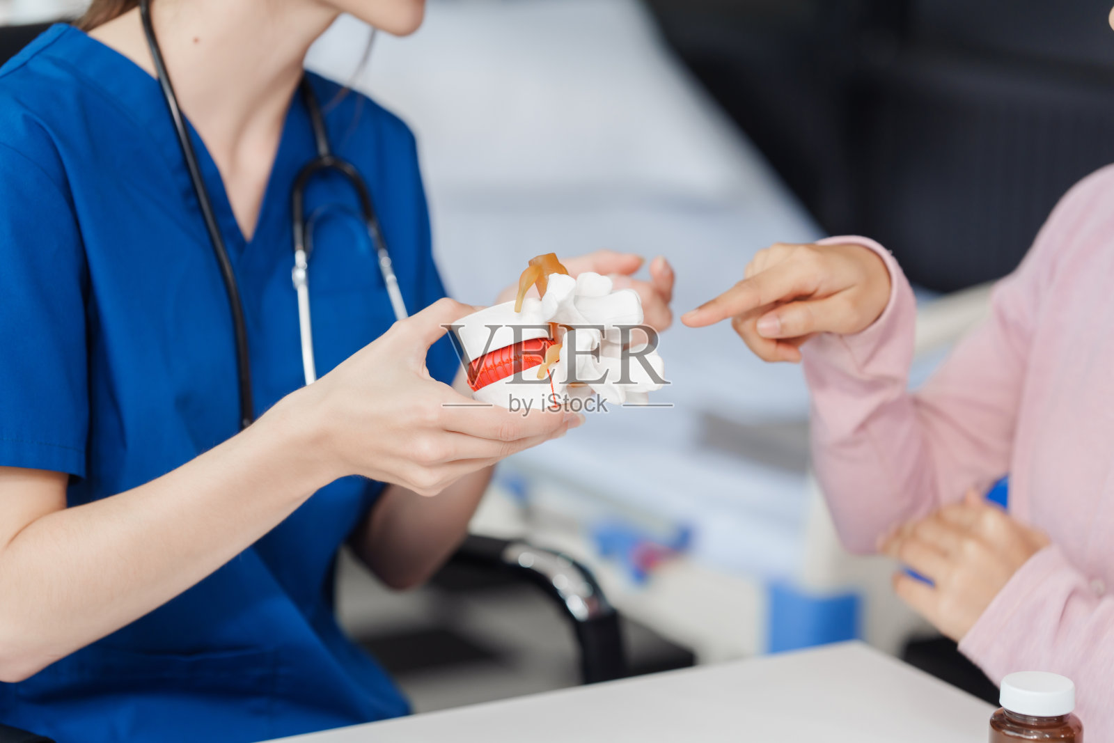 白种女医生在医务室办公桌上,借助医学辅助解剖仪器,向亚洲女性患者讲解人体腰椎间盘突出解剖模型照片摄影图片