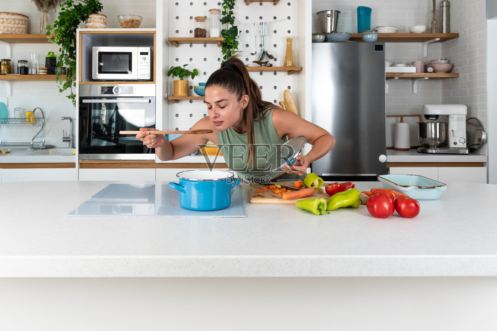 年轻的运动女性在月经期间准备健康餐。女性在月经期间在家庭厨房烹饪蔬菜。健康饮食搭配有机食品,午餐后在家锻炼照片摄影图片