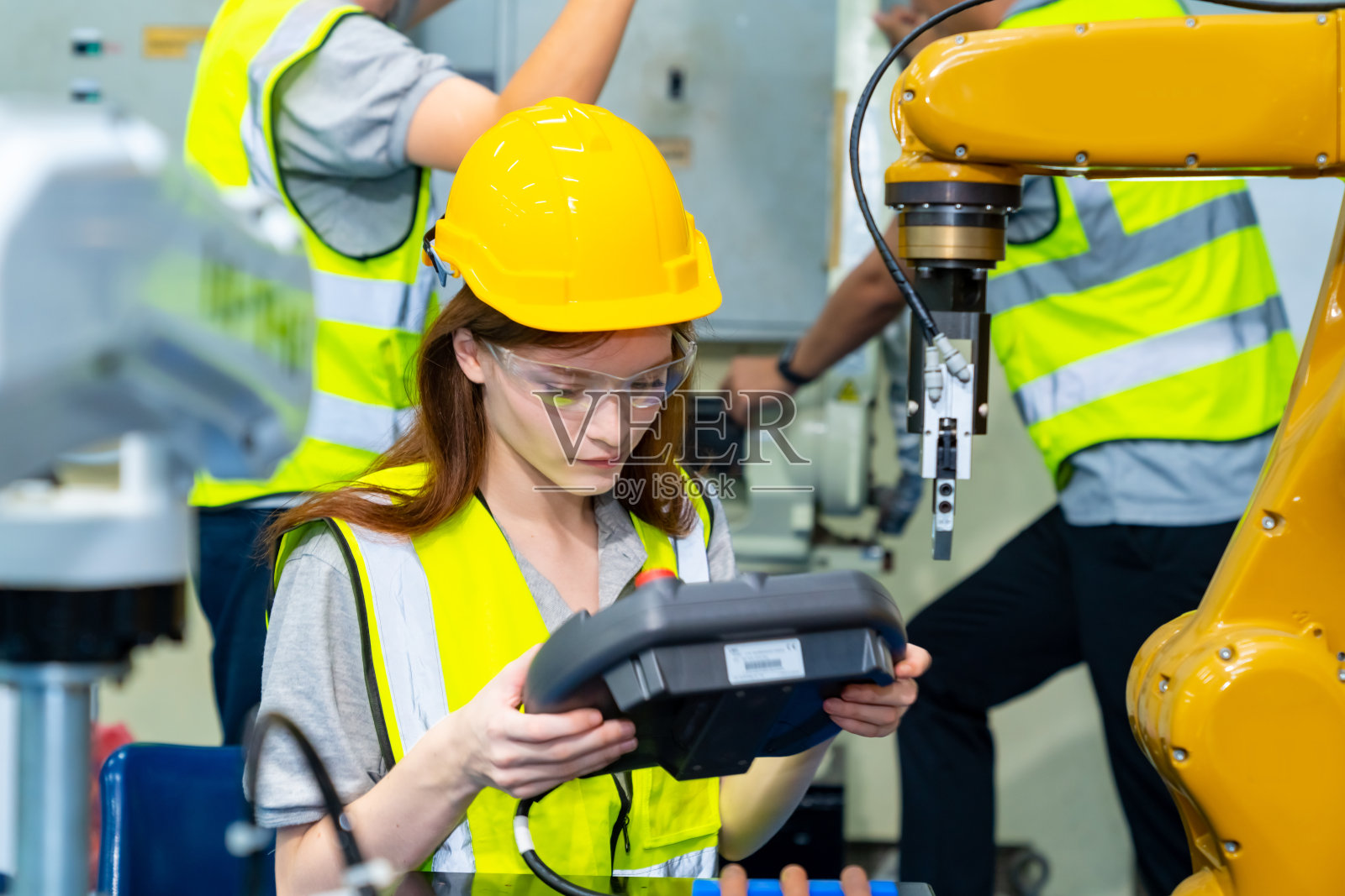 在工厂里操作机器人的女工程师。照片摄影图片