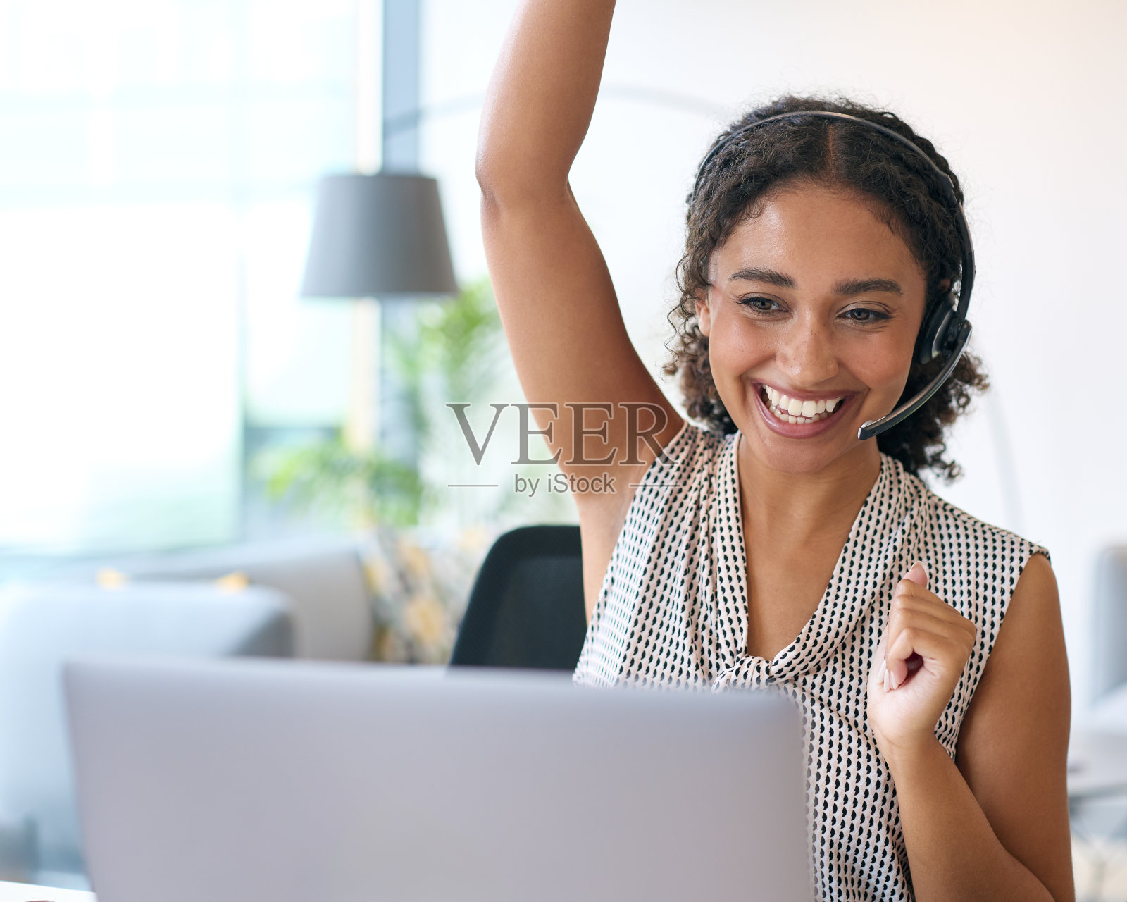 戴耳机的女人坐在办公桌前用笔记本电脑庆祝好消息或达到销售目标照片摄影图片