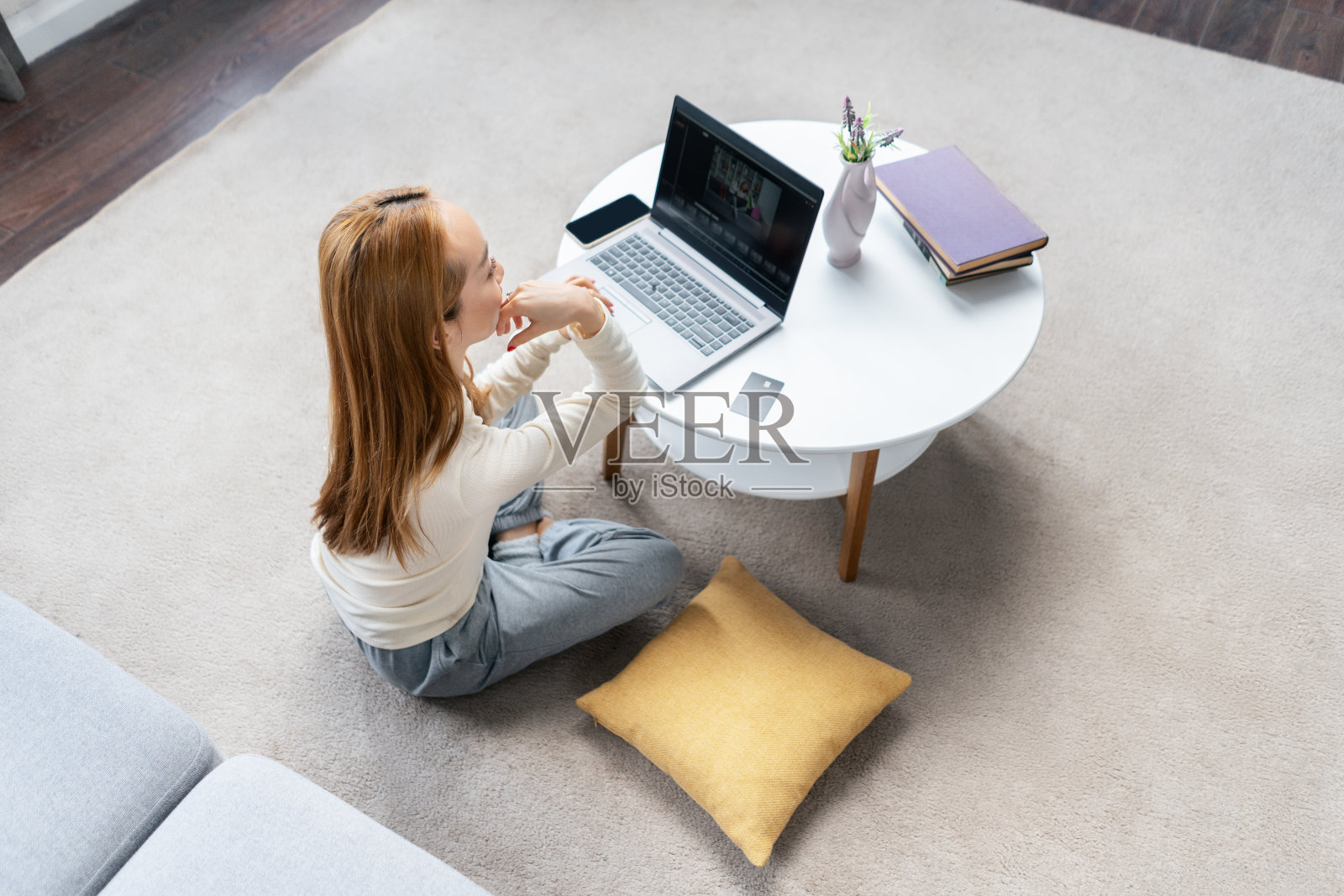年轻女子在地板上放松,手里拿着笔记本电脑和书照片摄影图片