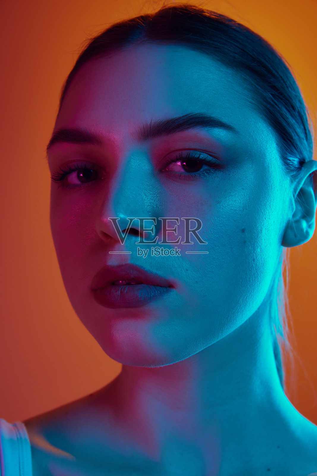 在渐变背景下的粉蓝混合霓虹灯下,一头黑发的年轻女子的特写肖像。照片摄影图片