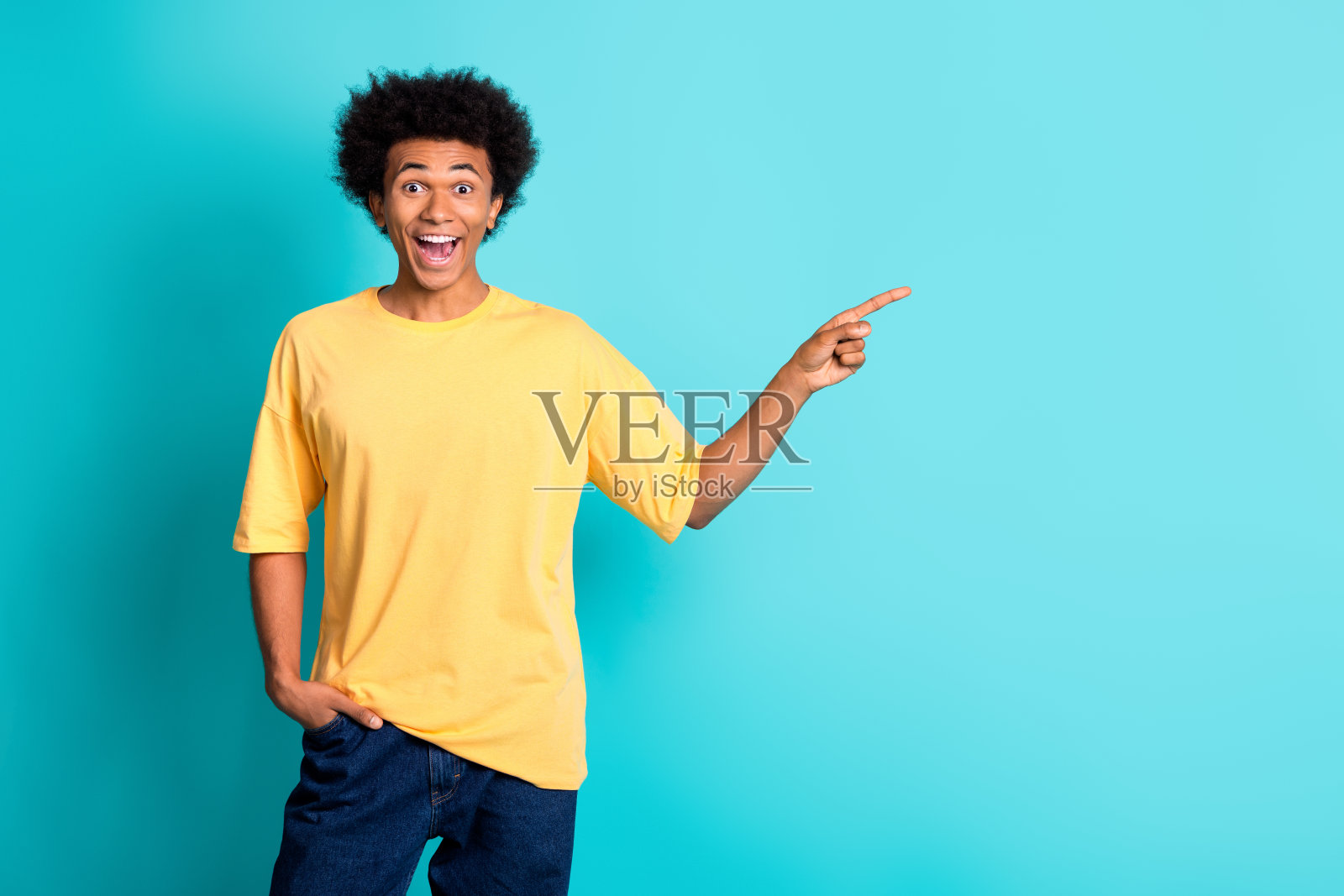 一个留着非洲式发型、穿着大号t恤的欣喜若狂的男人的照片,在蓝绿色的背景上指向命题的空白空间照片摄影图片