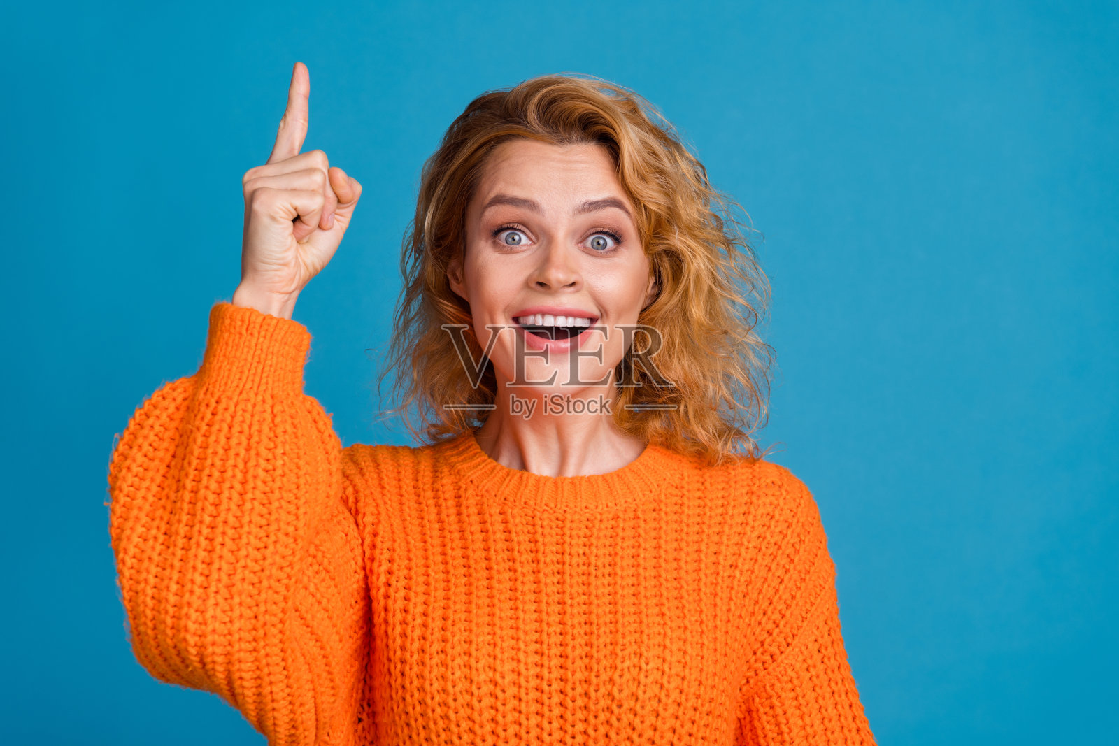 照片中快乐开朗的女人穿着时髦的橙色衣服,双手乳房好心情孤立在蓝色的背景照片摄影图片