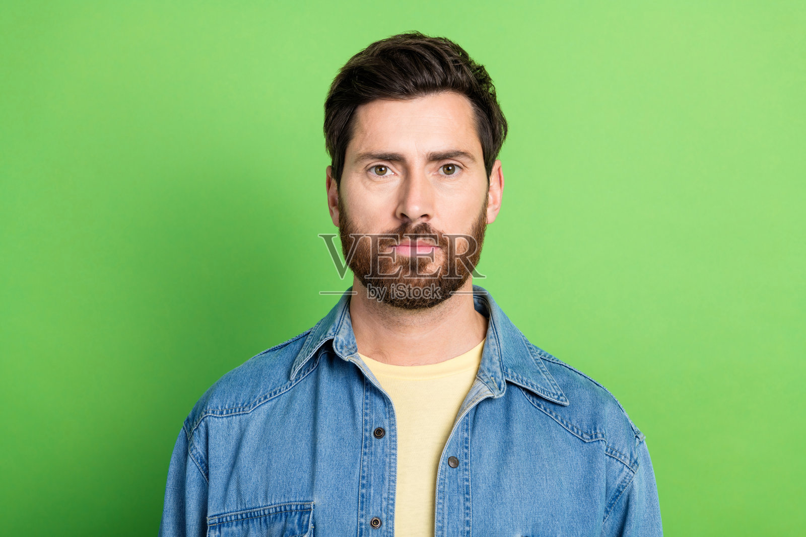 照片中,严肃自信的小伙子穿着牛仔裤衬衫,空白空间孤立绿色背景照片摄影图片