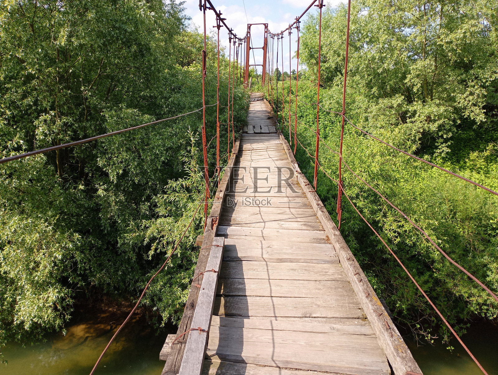 一座用生锈的旧缆索架设的木桥和用旧木板搭建的木面横跨着清澈的河水。一座横跨水库的漂亮的桥,供行人使用。照片摄影图片