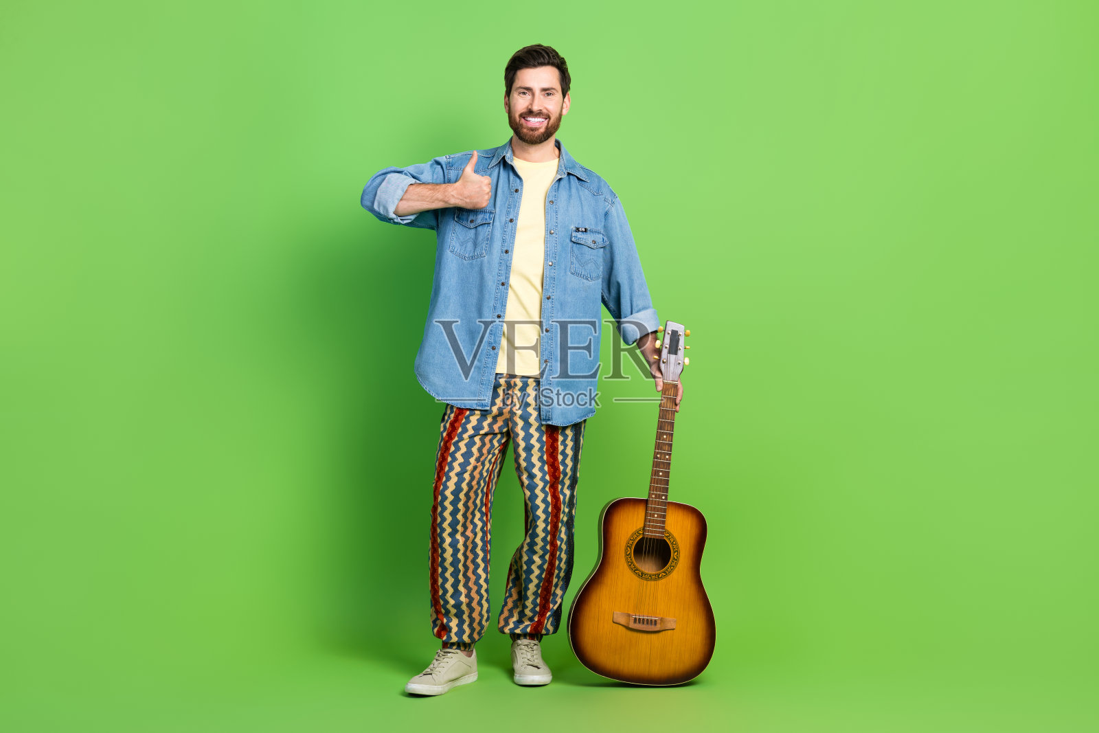 自信积极的人穿着牛仔裤衬衫的全长照片显示拇指向上享受吉他音乐孤立的绿色背景照片摄影图片