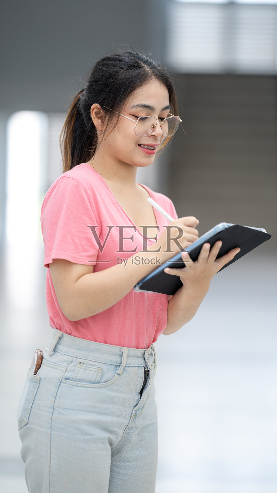 一个穿粉红色衬衫和牛仔裤的女人正在写字板上写字照片摄影图片