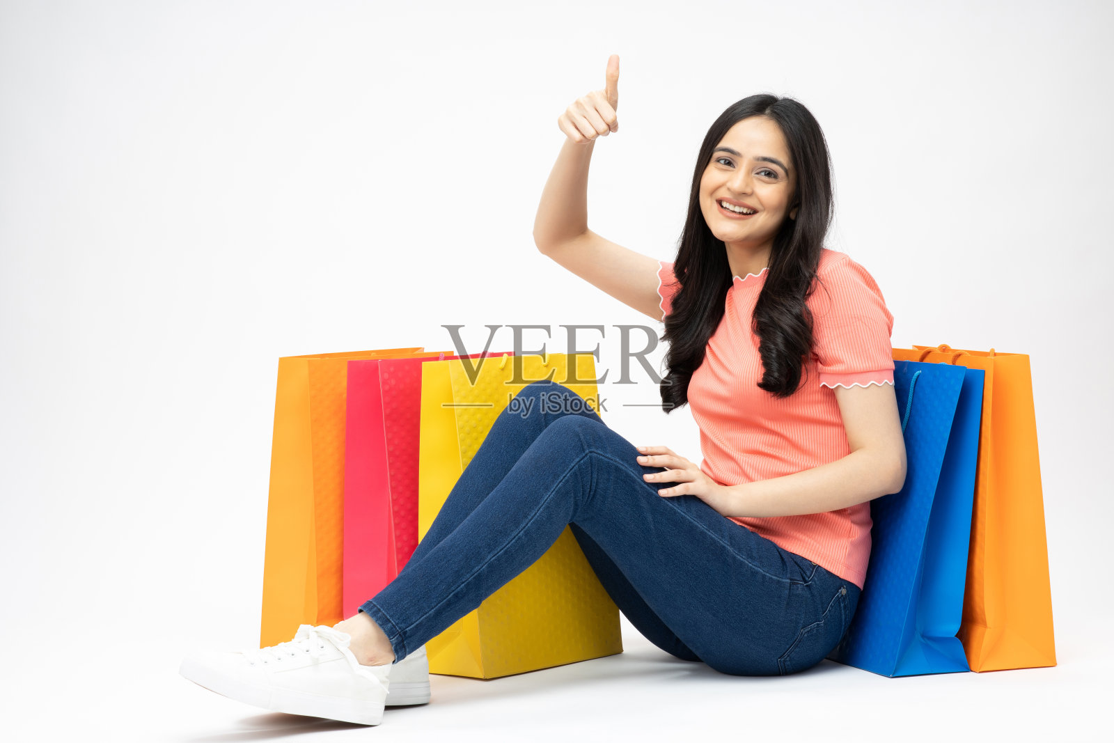 年轻女孩的全身肖像坐在拿着购物袋开朗孤立的白色背景股票照片照片摄影图片