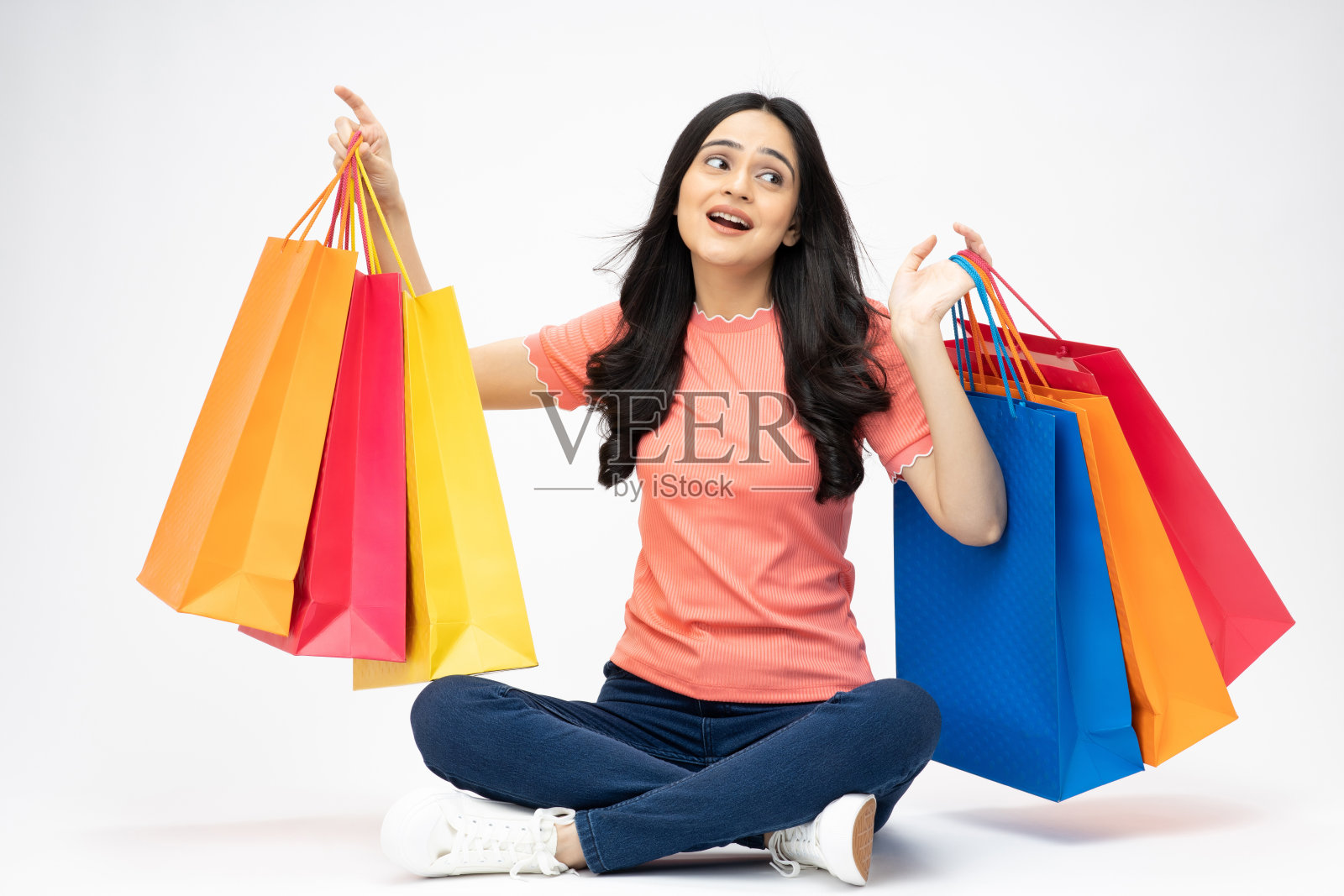 年轻女孩的全身肖像坐在拿着购物袋开朗孤立的白色背景股票照片照片摄影图片