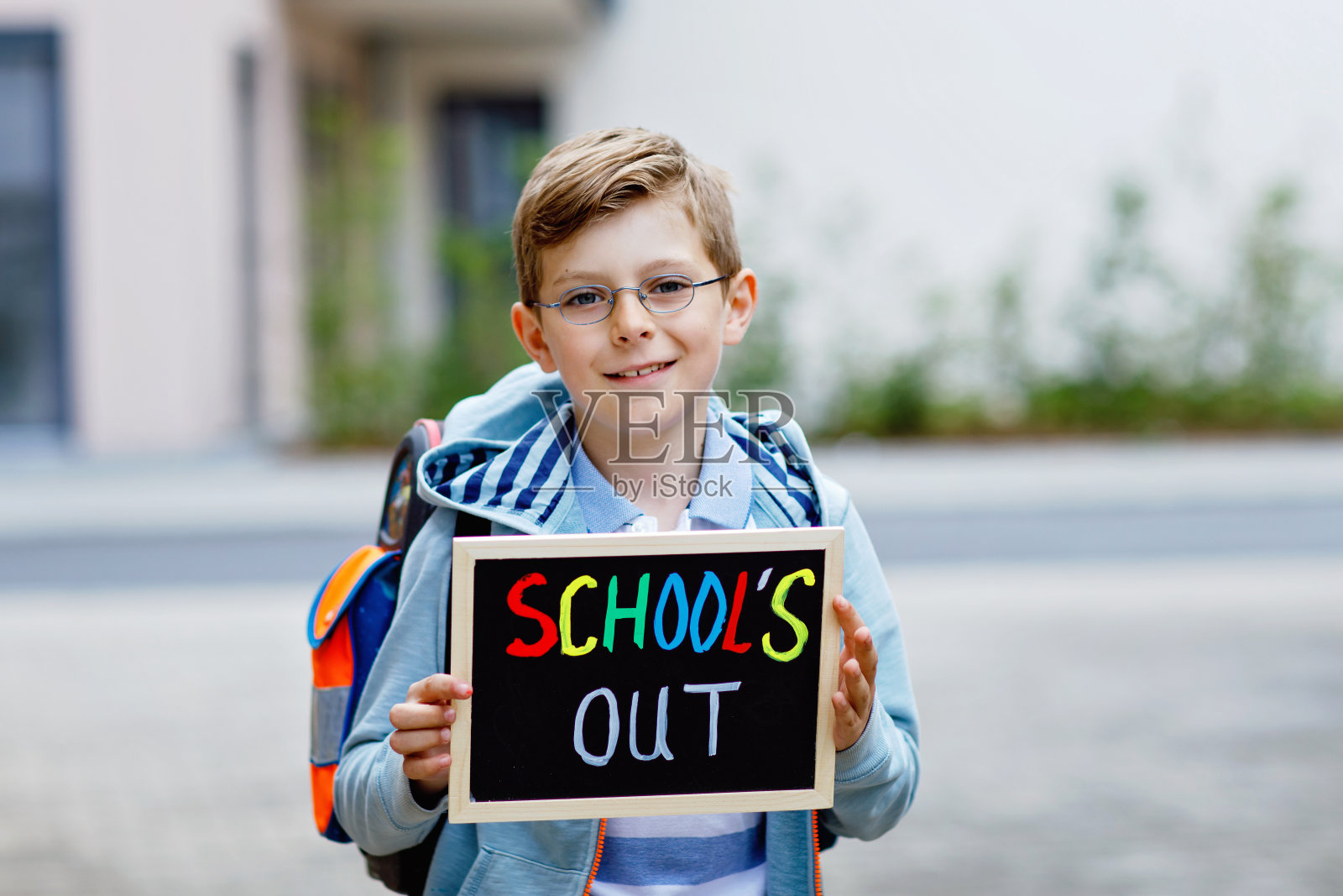 快乐的小男孩背着背包或挎包。上学路上的小学生。健康可爱的孩子在户外,还有粉笔桌作为文案空间。要么回学校,要么退学。照片摄影图片