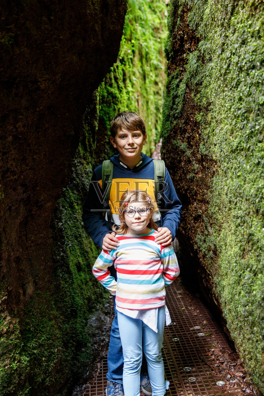 十几岁的男孩背着背包和一个学龄前的小女孩徒步穿过一个山洞。快乐的孩子,兄弟姐妹,玩得开心。照片摄影图片
