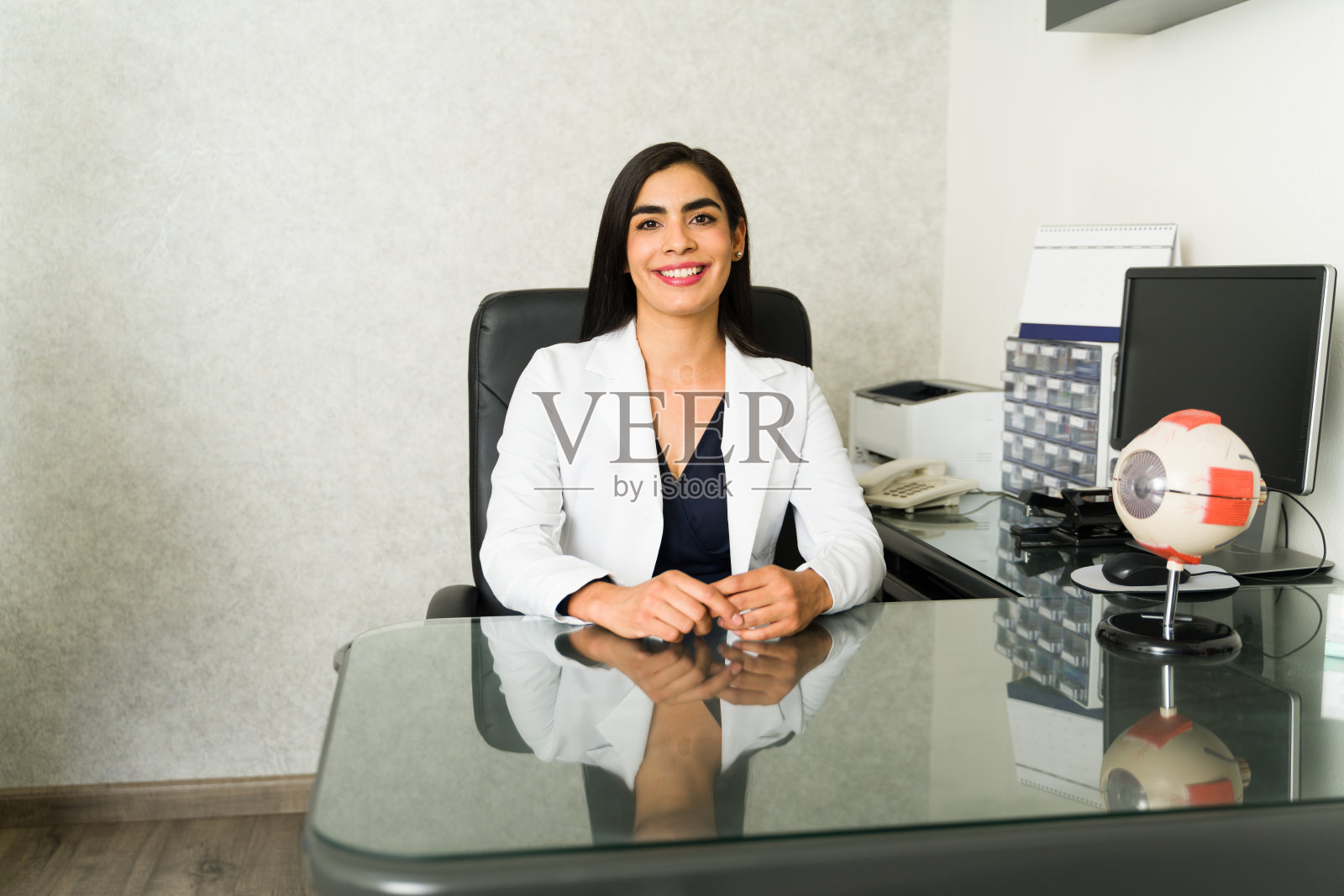 在一家现代诊所里,一位女眼科医生和一位眼部模特坐在办公桌前,流露出自信和友好照片摄影图片