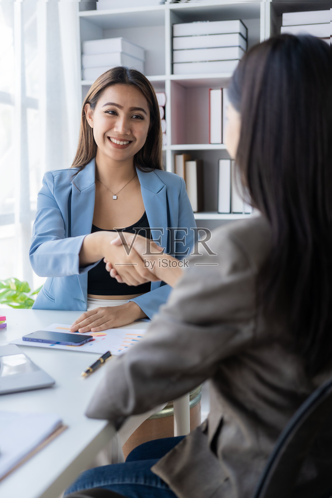 两位亚洲女企业家在联合金融业务和投资公司的业务上取得了成功,她们互相握手祝贺。照片摄影图片