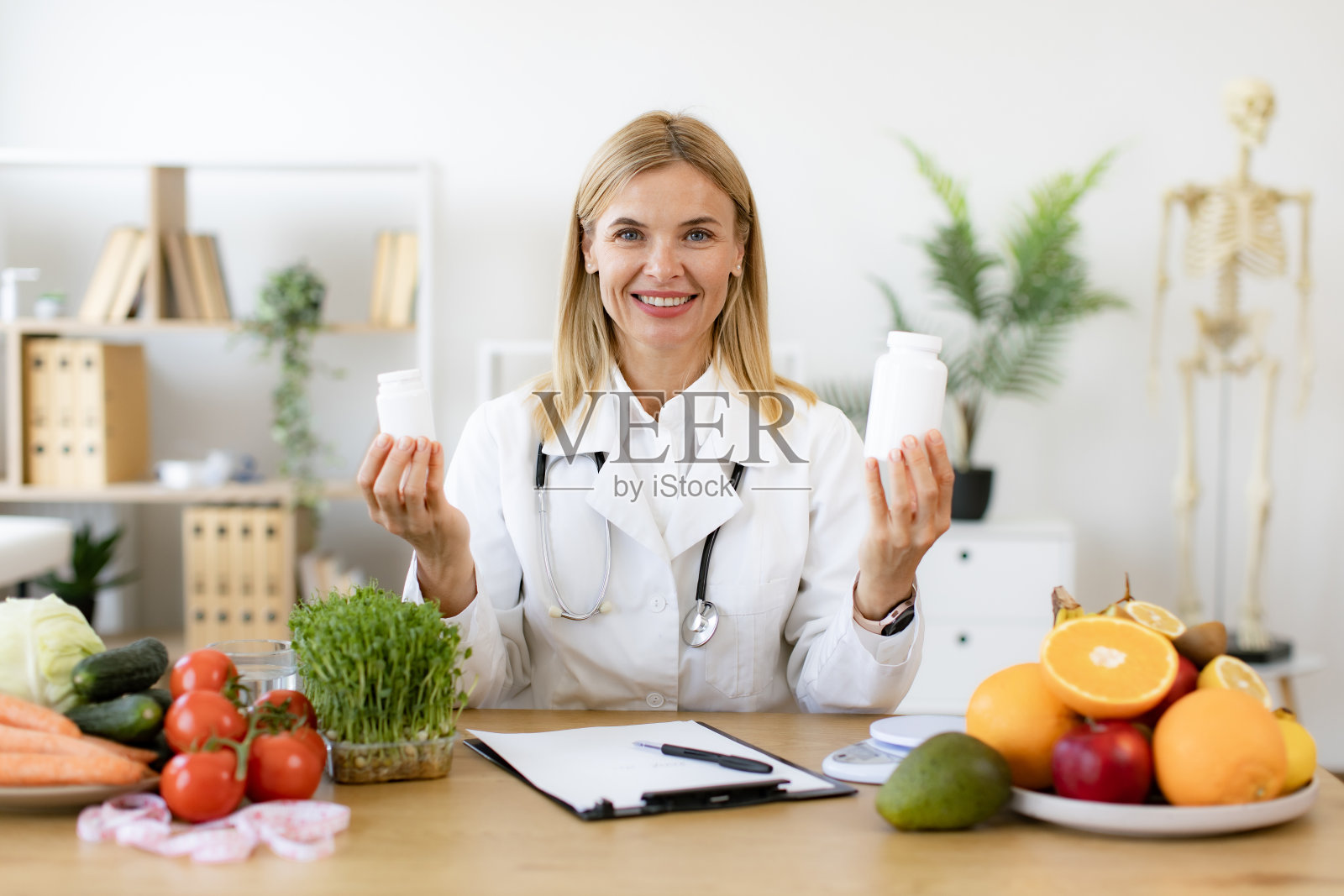 穿着实验室大褂的白人女士在展示药瓶时对着镜头微笑。照片摄影图片