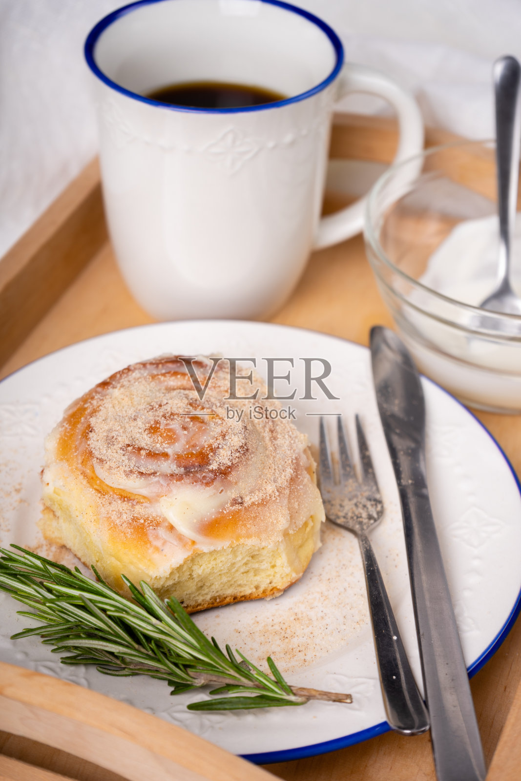 用迷迭香和一杯茶装饰的白色陶瓷盘子上的自制肉桂卷照片摄影图片