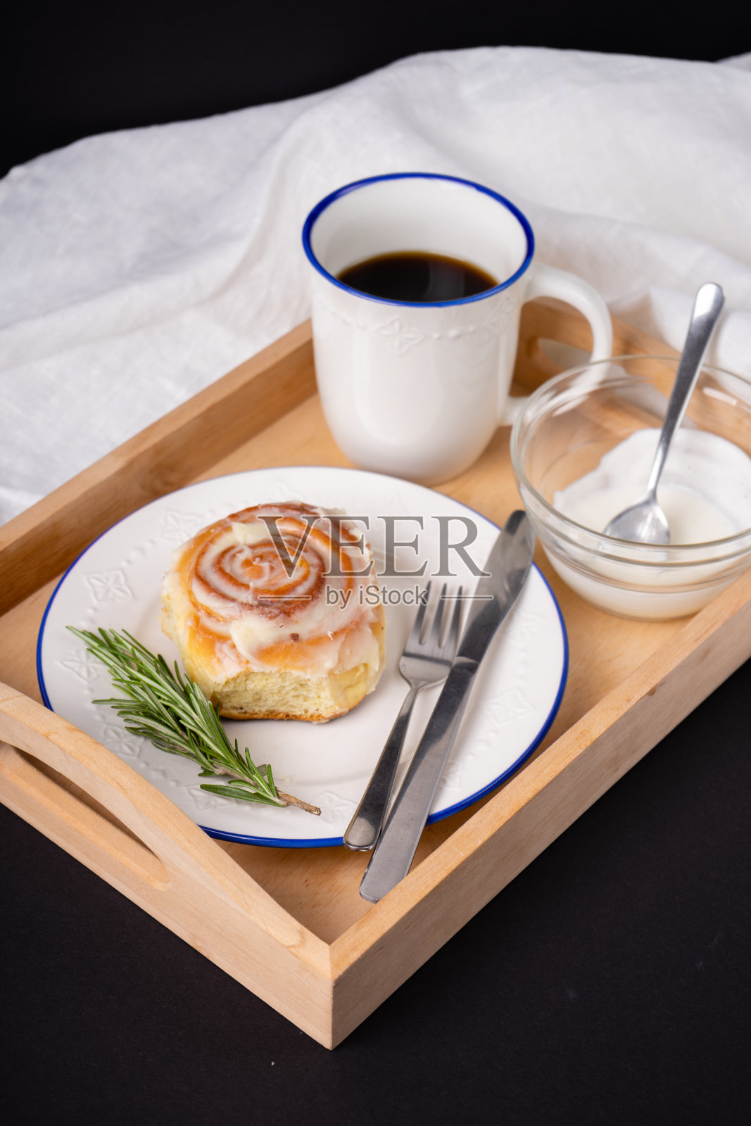 用迷迭香和一杯茶装饰的白色陶瓷盘子上的自制肉桂卷照片摄影图片