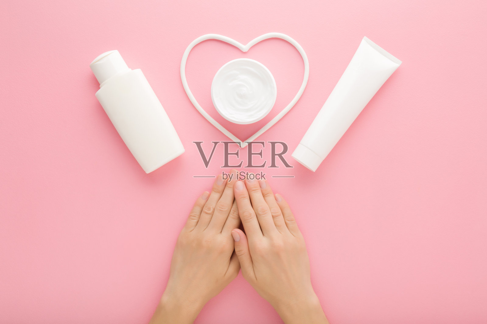 年轻的成年妇女的手,白色的奶油罐,瓶子,管和心形在粉红色的桌子背景。柔和的颜色。呵护干净柔软的女性身体肌肤。特写镜头。视角镜头。自顶向下视图。照片摄影图片