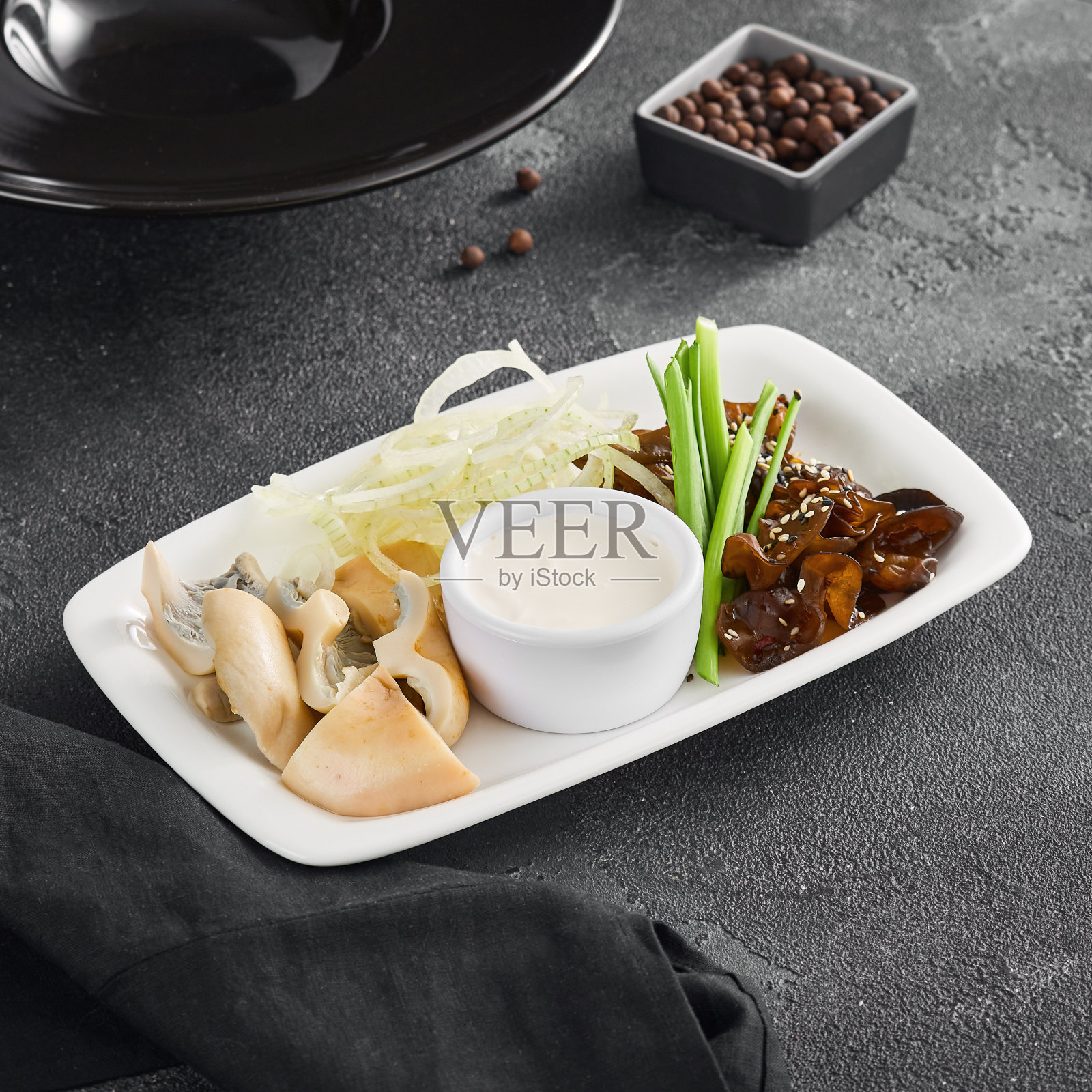 美味的腌蘑菇、切成薄片的洋葱、新鲜的大葱和奶油蘸酱,优雅地放在白色矩形盘子上照片摄影图片