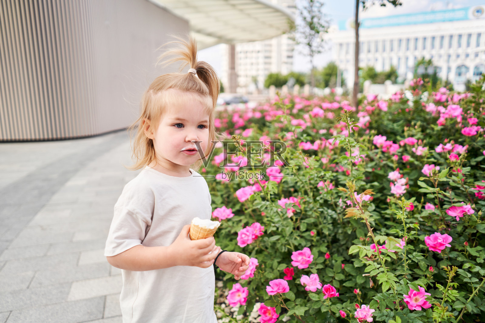 饥饿的孩子喜欢在户外吃冰淇淋。一个可爱的婴儿的肖像,脏兮兮的脸舔着奶油冰淇淋,在城市公园散步,户外活动。照片摄影图片