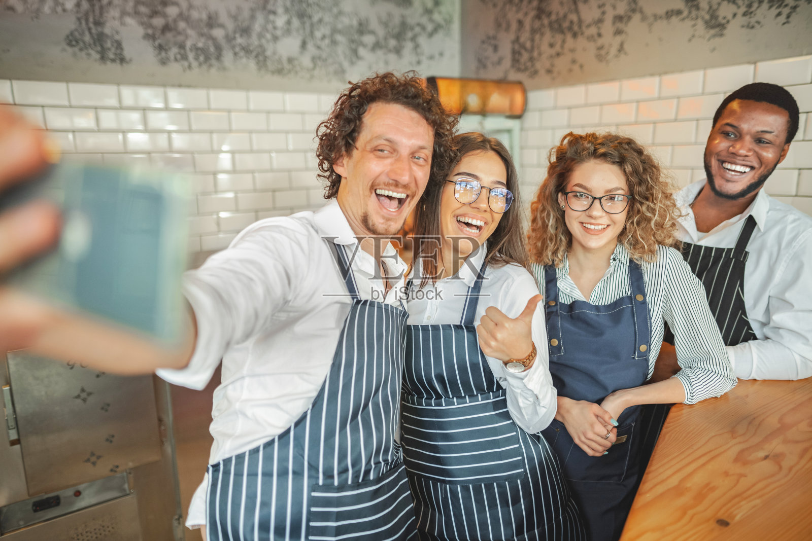 一群穿着围裙的多种族员工在吧台后面兴奋地自拍照片摄影图片
