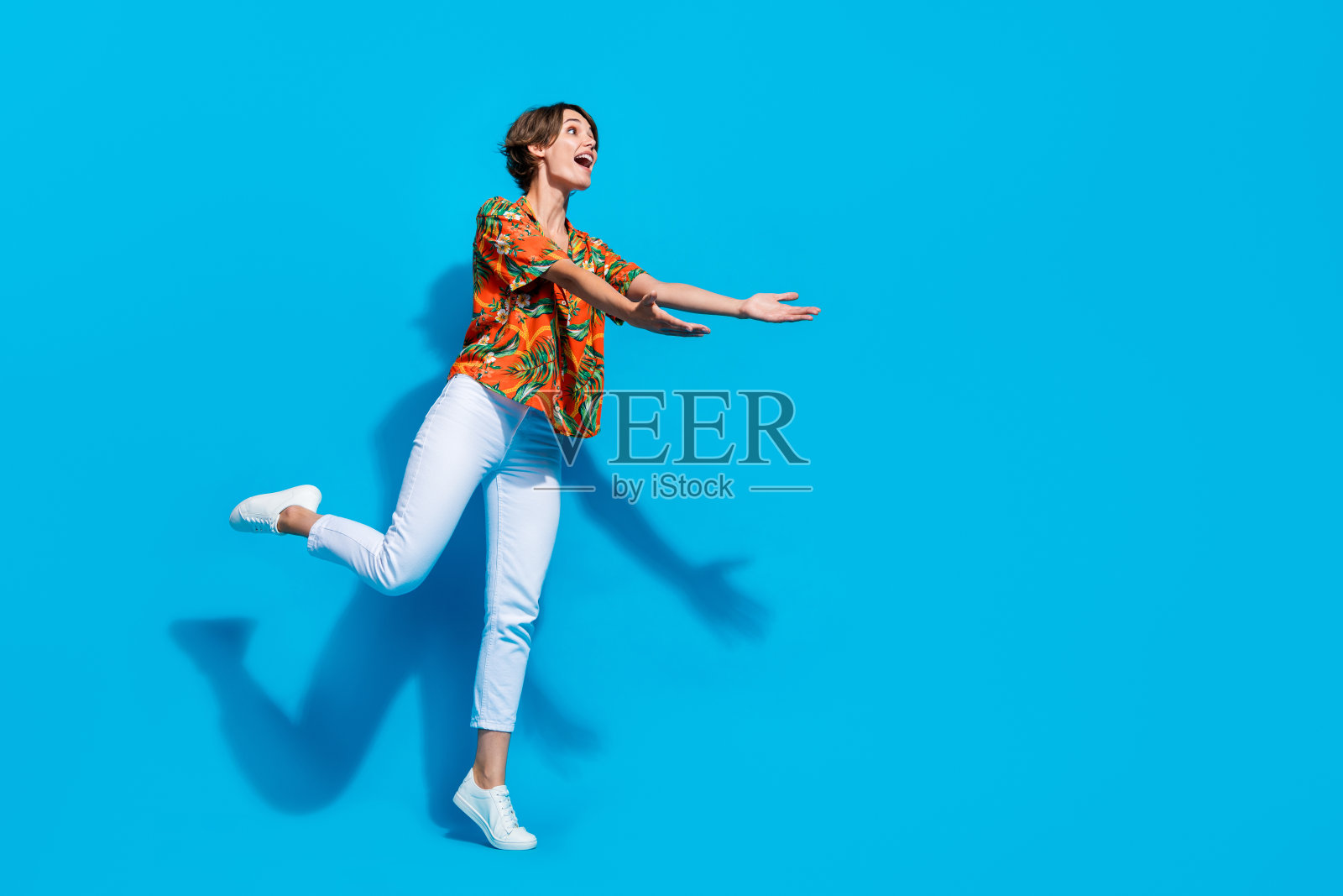 女孩穿着时髦的热带印花衣服,遮住耳朵,在蓝色的背景上避免嘈杂的噪音照片摄影图片