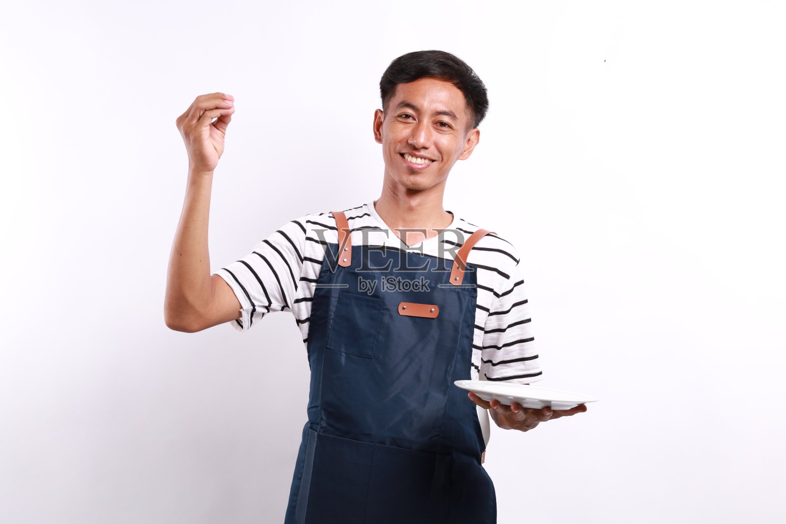 烹饪,烹饪和人的概念-快乐微笑的亚洲人在围裙上拿着空盘子,在白色背景上显示美食标志照片摄影图片