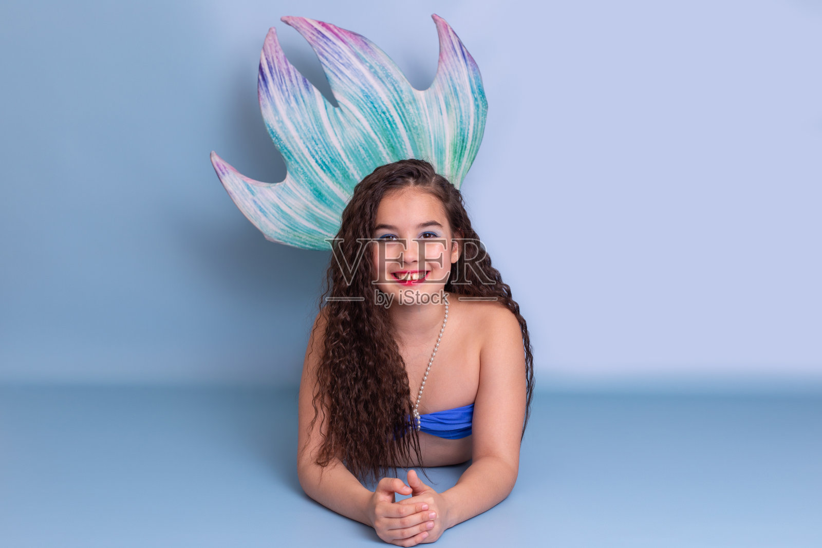穿着美人鱼服装的美丽女孩躺在浅蓝色的背景上照片摄影图片