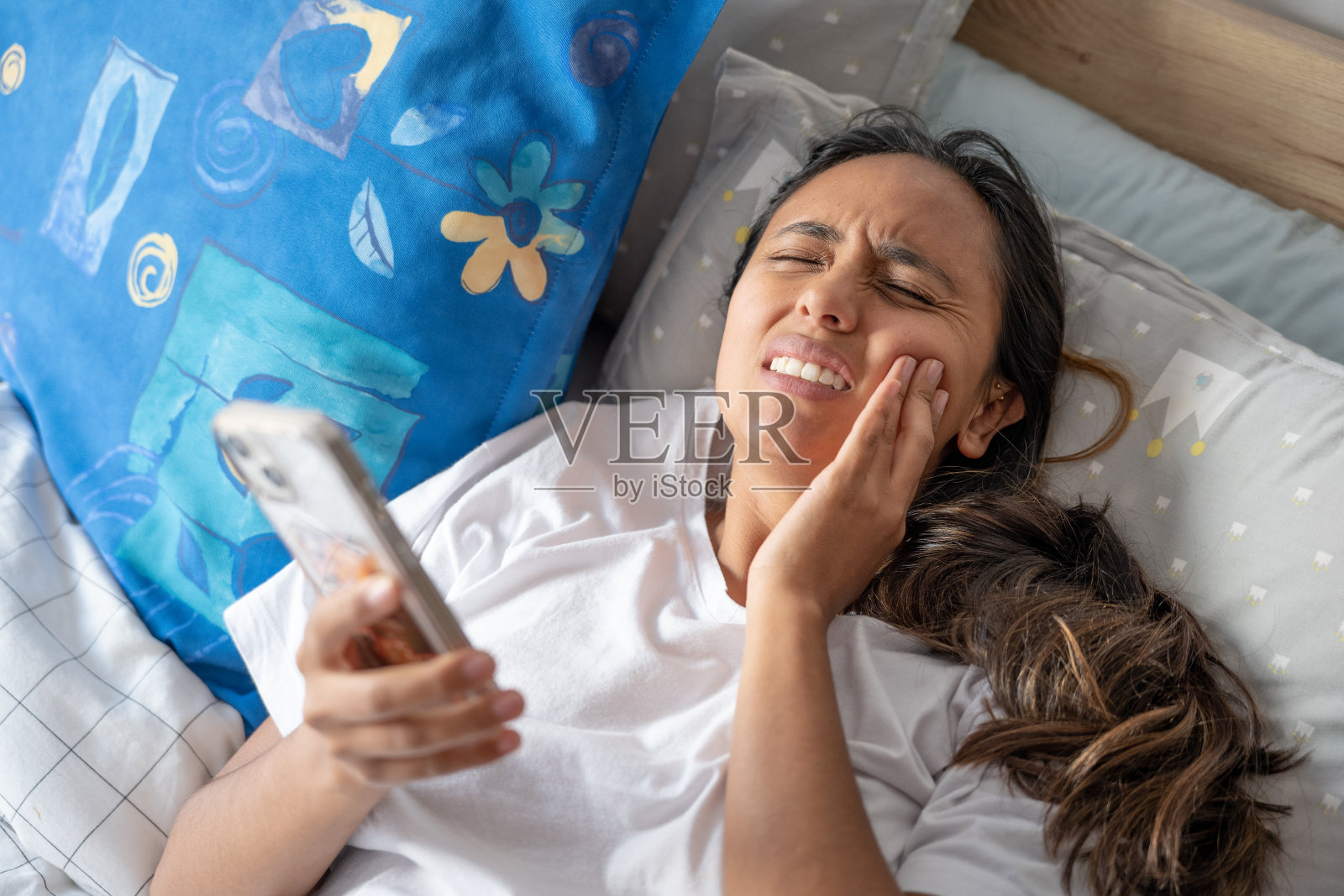 一个牙齿疼痛的年轻女人白天穿着睡衣躺在她房间的床上照片摄影图片