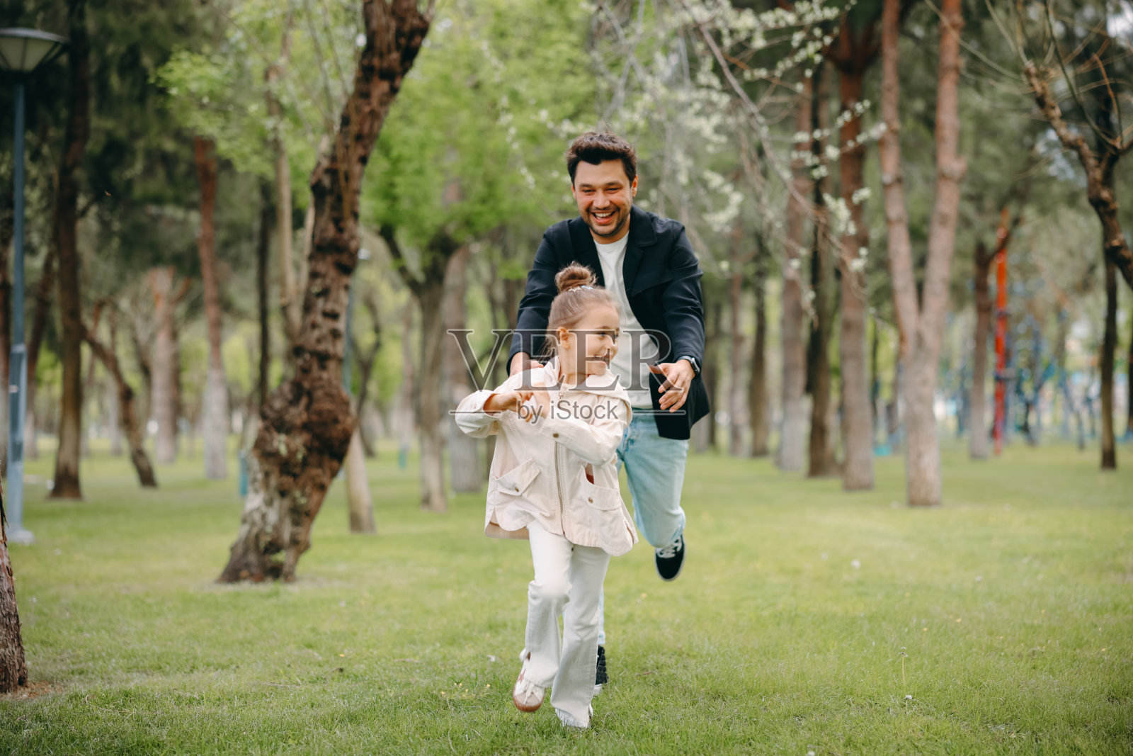 无忧无虑的年轻父亲和女儿在奔跑的春日里散步。照片摄影图片