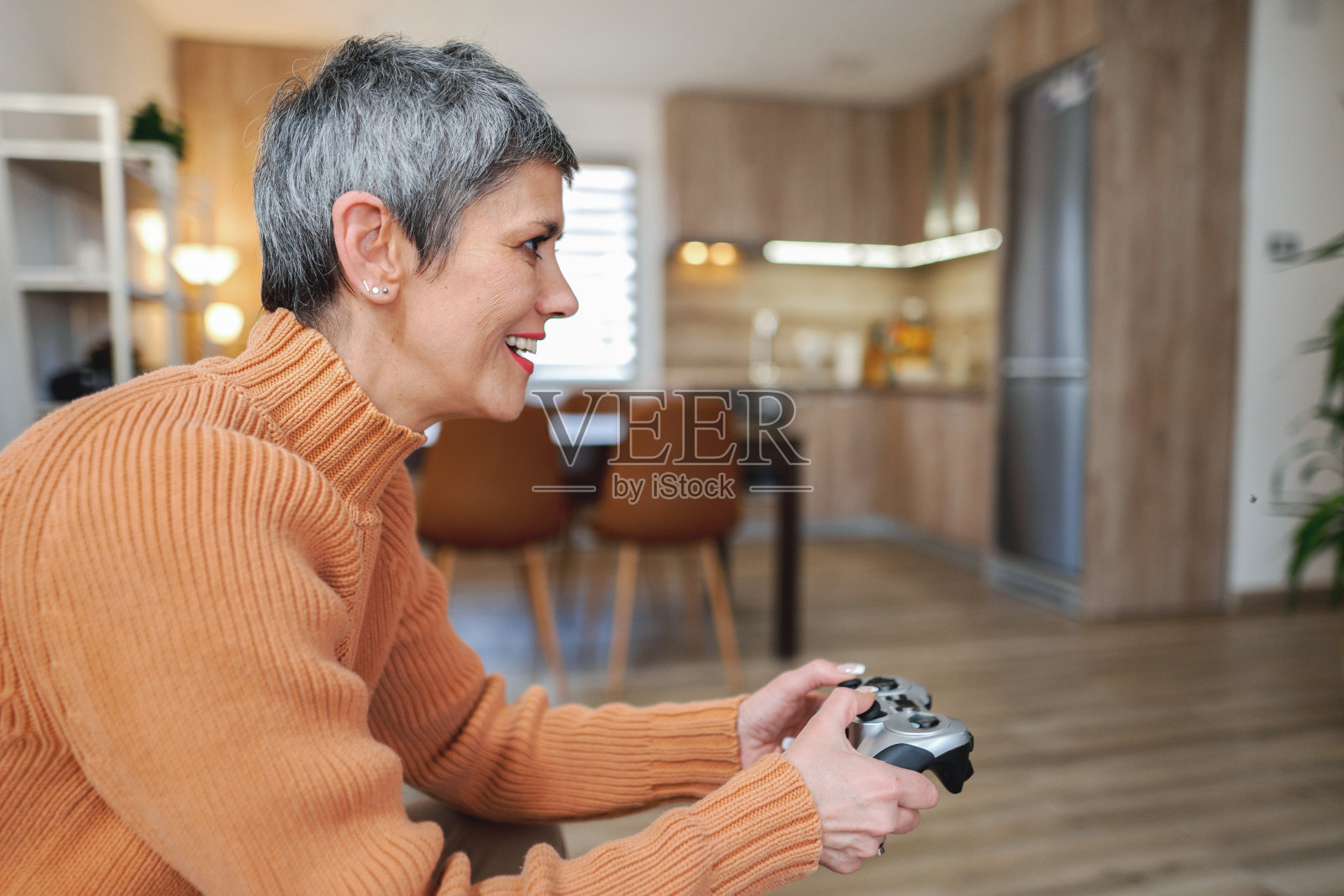 争强好胜、头发灰白的成熟的女人在客厅里玩电子游戏照片摄影图片
