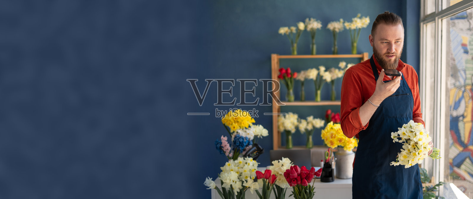 男花商用智能手机录制音频信息,在网上与客户聊天,站在花店里提供咨询照片摄影图片