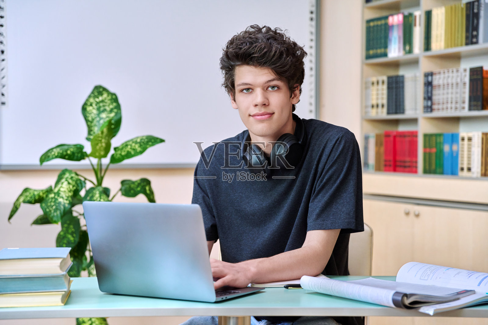 在教育图书馆里,一个大学生拿着笔记本电脑坐在书桌前照片摄影图片