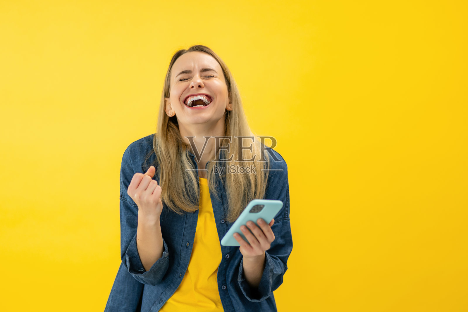 是的,好消息。兴奋的女人庆祝胜利的肖像,使用智能手机,微笑的年轻女士成功,拿着手机,黄色工作室背景照片摄影图片