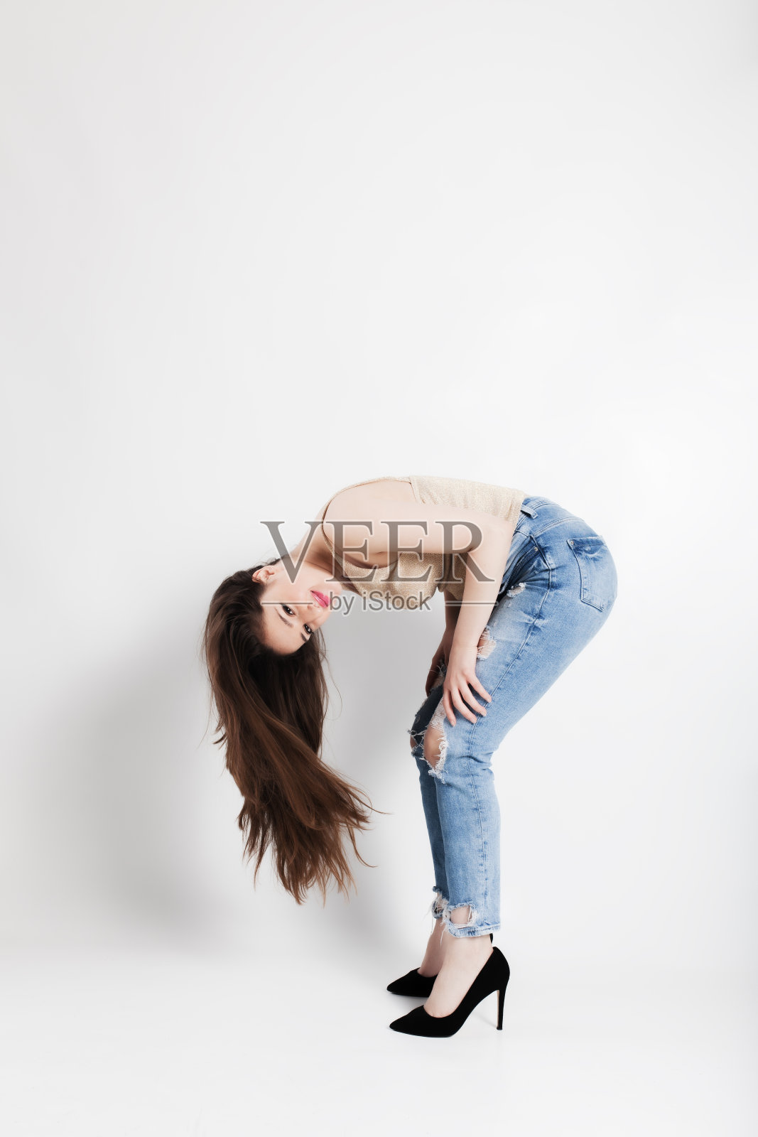 年轻女子穿着时尚的破洞牛仔裤和高跟鞋,在白色背景上表演后弯照片摄影图片