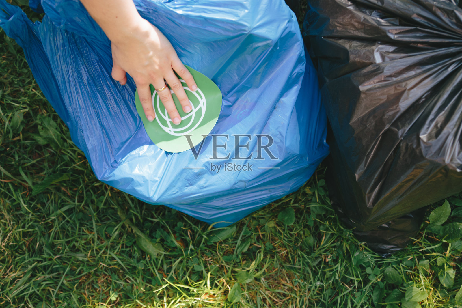 一只手把回收标签贴在蓝色垃圾袋上照片摄影图片