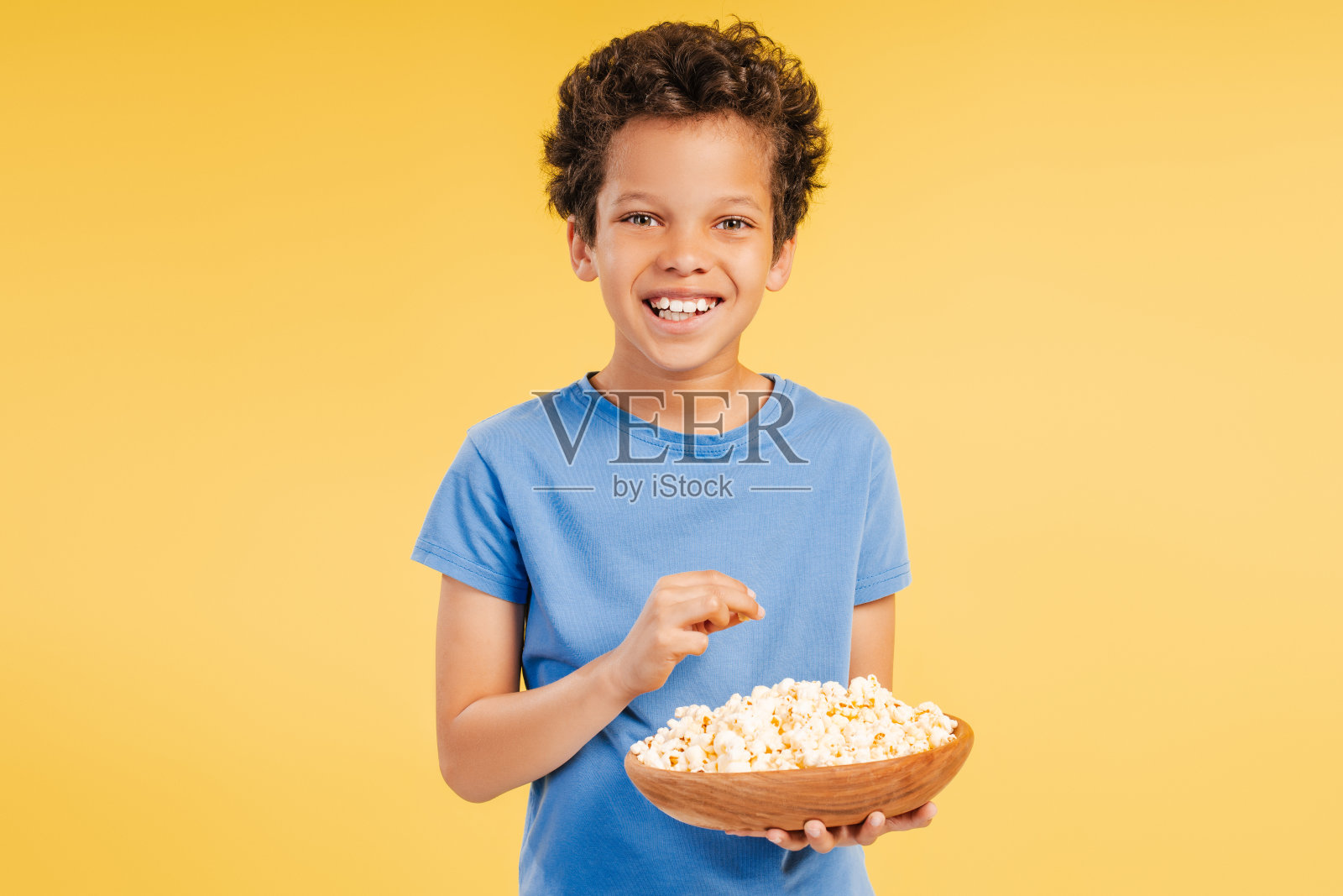 微笑英俊的非裔美国男孩看电影,吃爆米花,吃零食看着镜头照片摄影图片