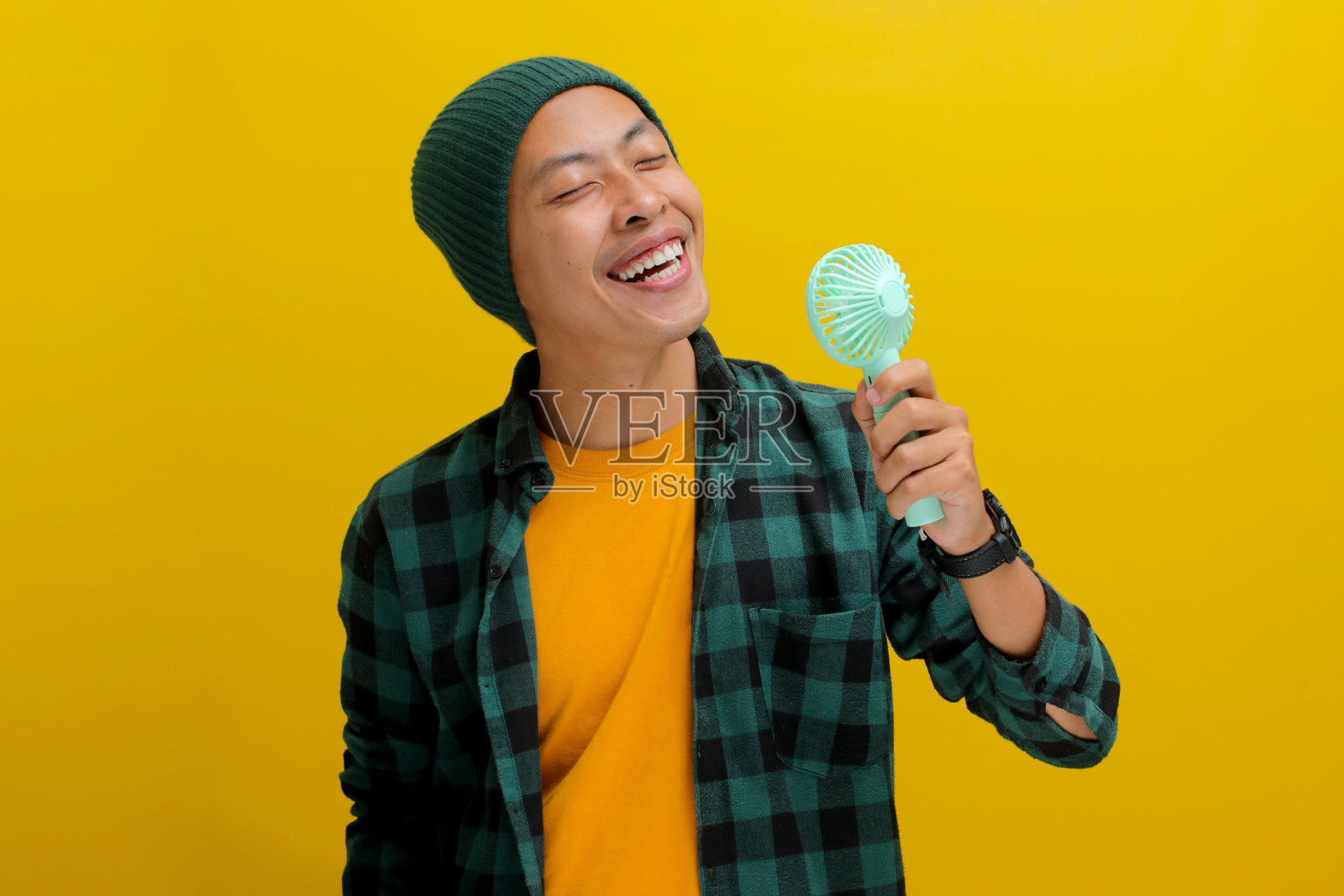 亚洲男人陶醉于从手持便携式迷你风扇的气流和清爽的凉风照片摄影图片